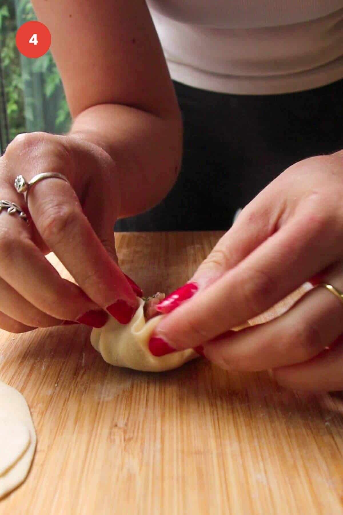 Hands folding dumpling on wooden board.