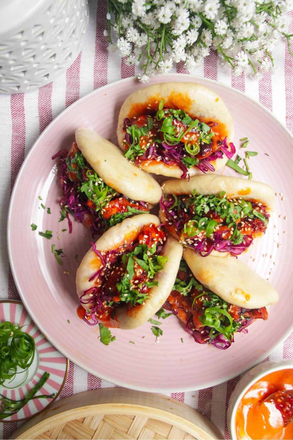 Five Korean chicken filled bao buns on a pink plate with aioli on the side.