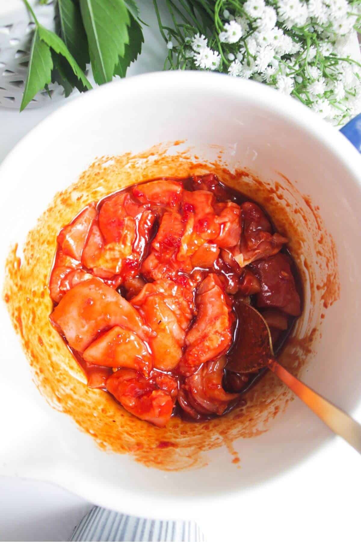 Chicken mixed through gochujang marinade in a mixing bowl.