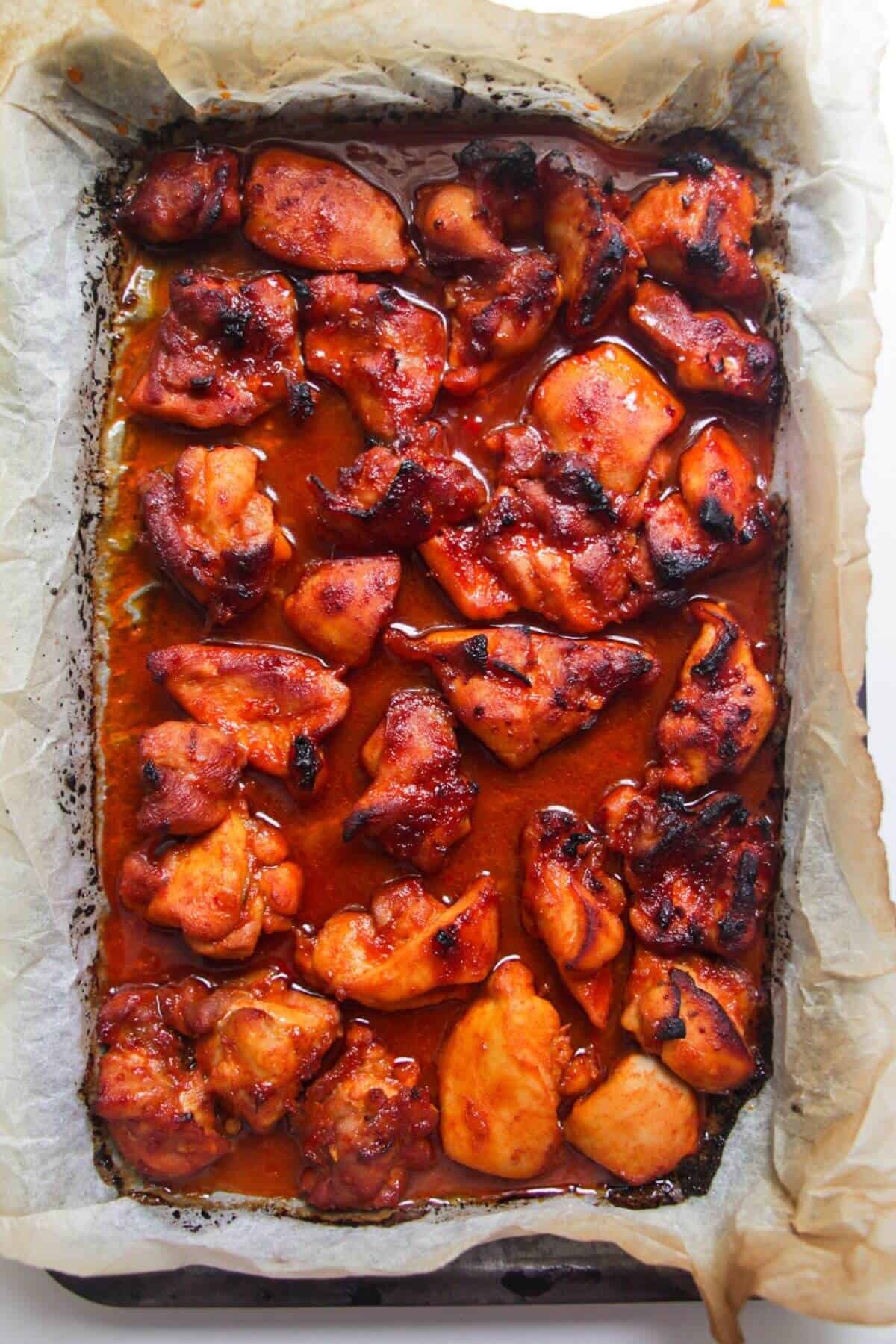 Charred gochujang chicken in a lined oven tray.