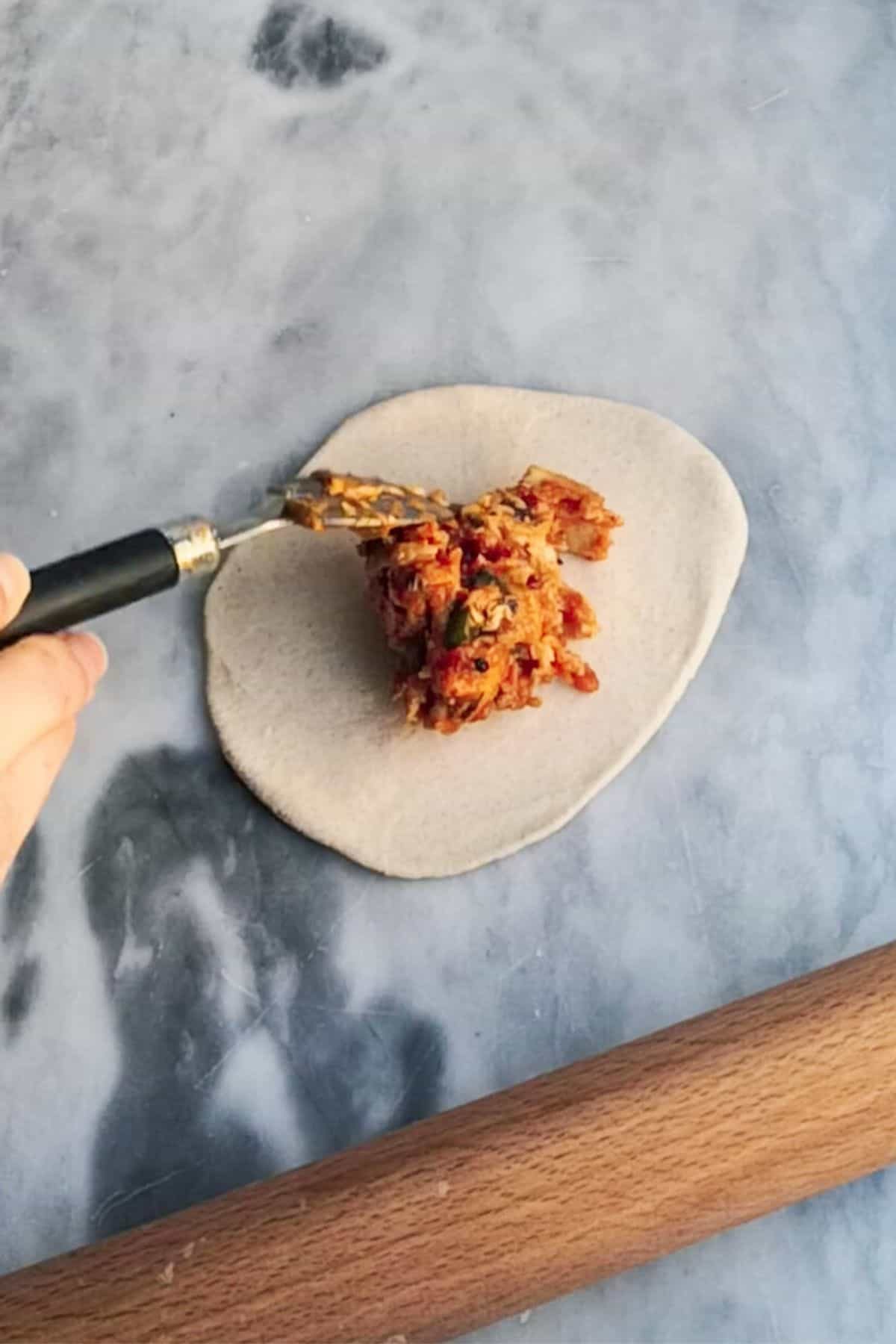 Small spoon adding sticky chicken mix to the middle of a dough circle.