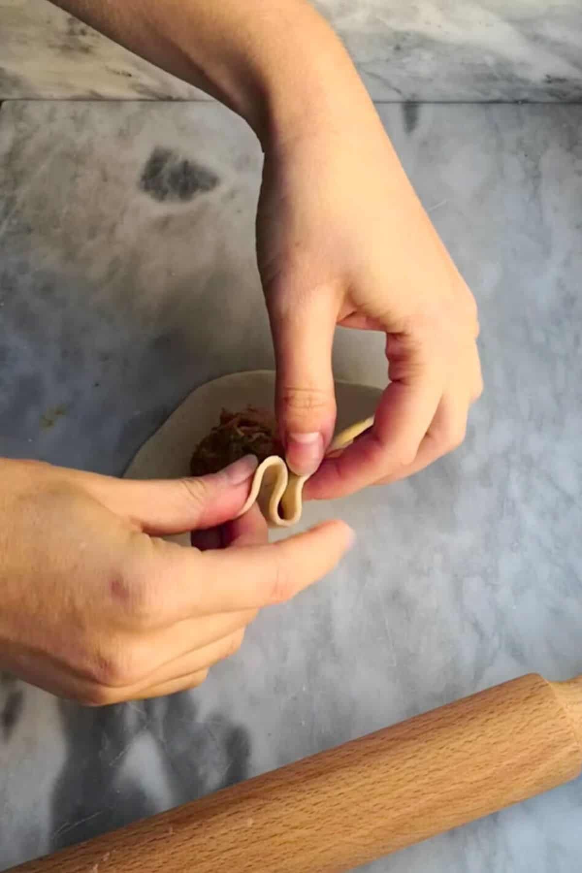 2 hands starting to pleat the steamed buns closed.