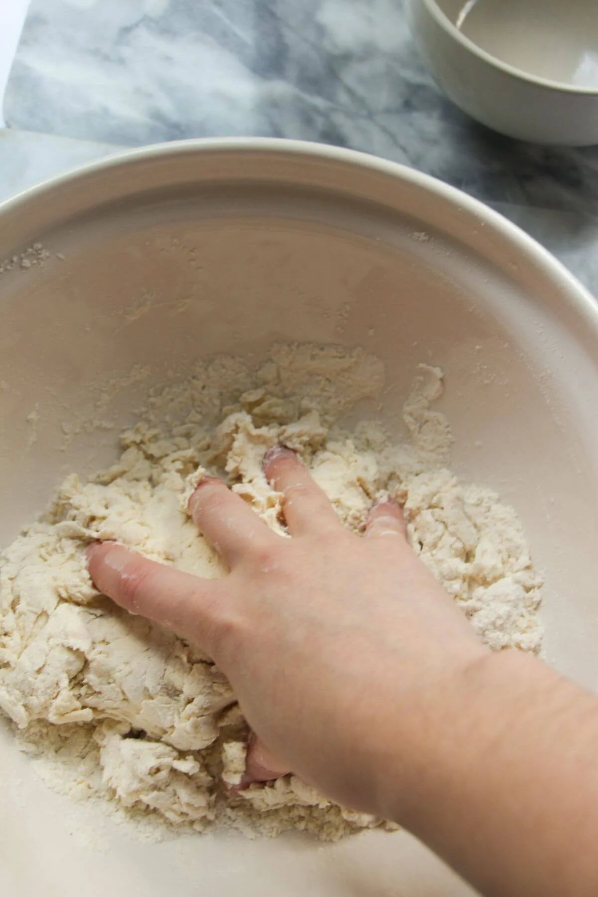 A hand squeezing flour and yogurt dough together in a large ceramic bowl.