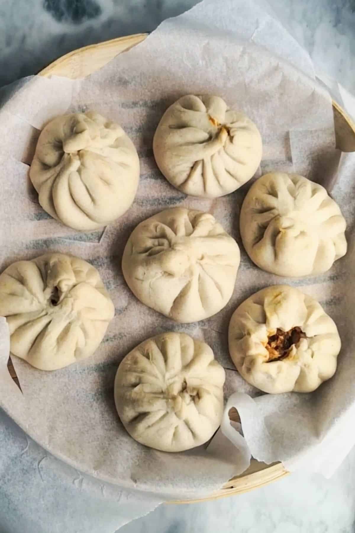 7 steamed buns in a lined bamboo steamer basket.