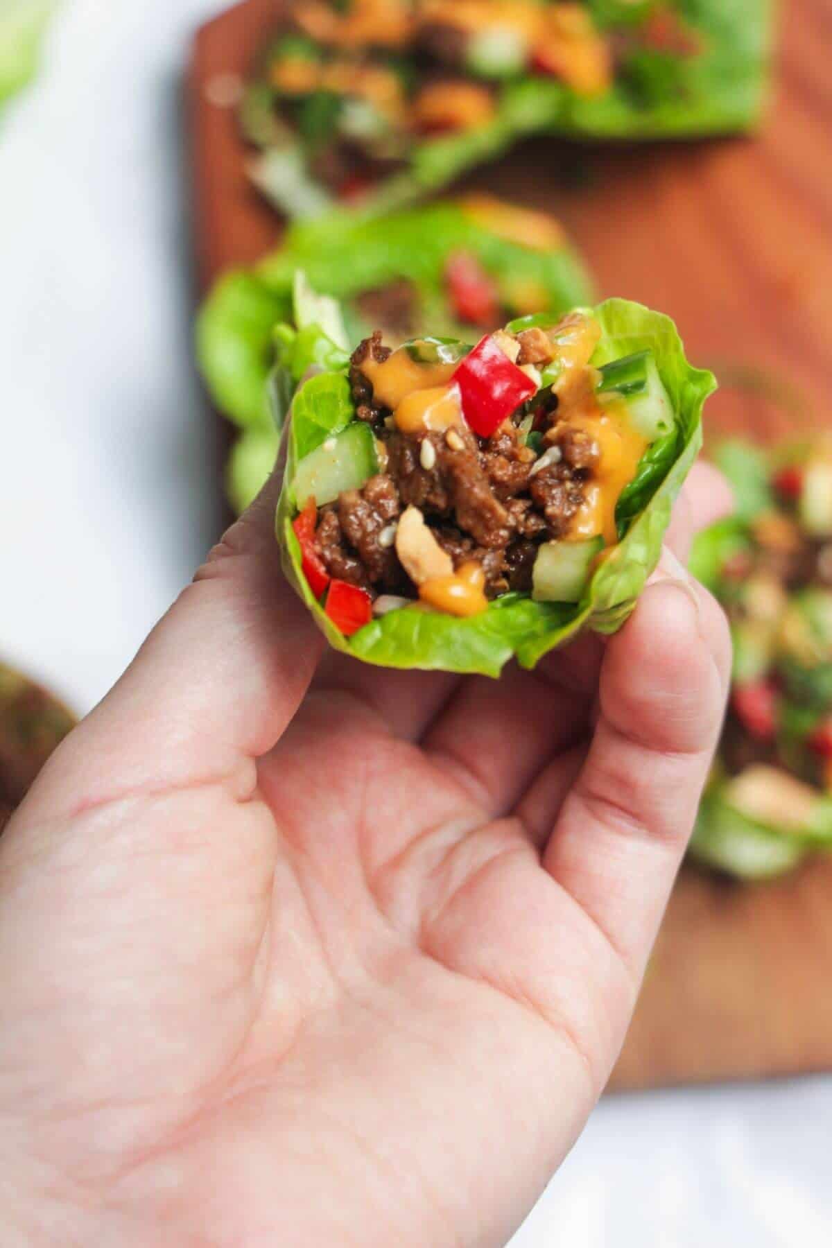 Hand holding Korean beef lettuce wrap with more wraps in the background.