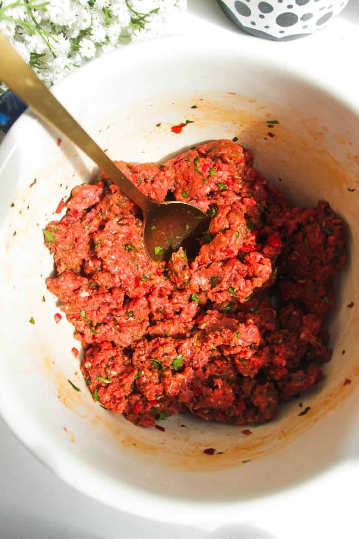 Spoon in a bowl with mixed lahmacun meat and seasoning.