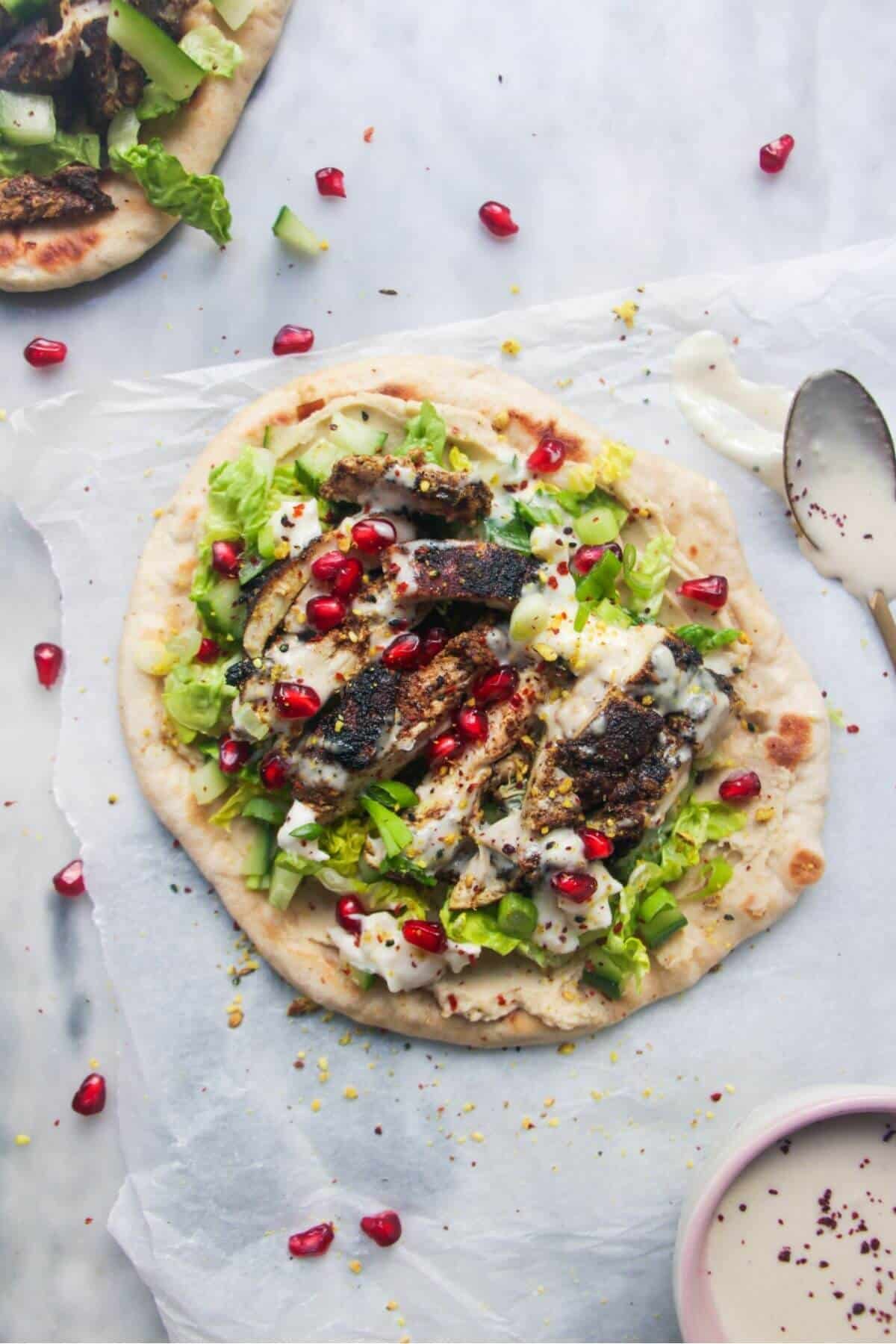 Chicken shawarma wrap on a grey marble background with a small bowl of tahini sauce on the side.