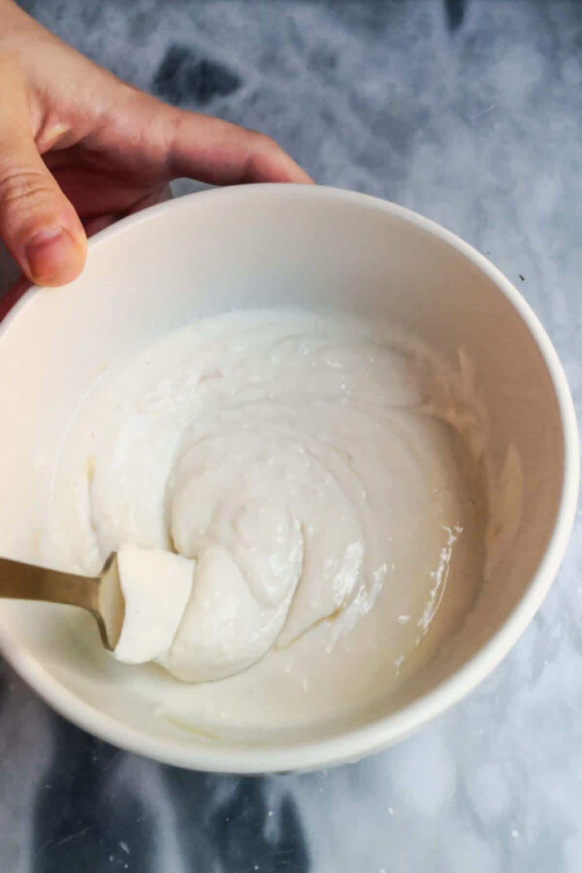 Yogurt tahini sauce mixed together in a small white bowl with a gold fork.
