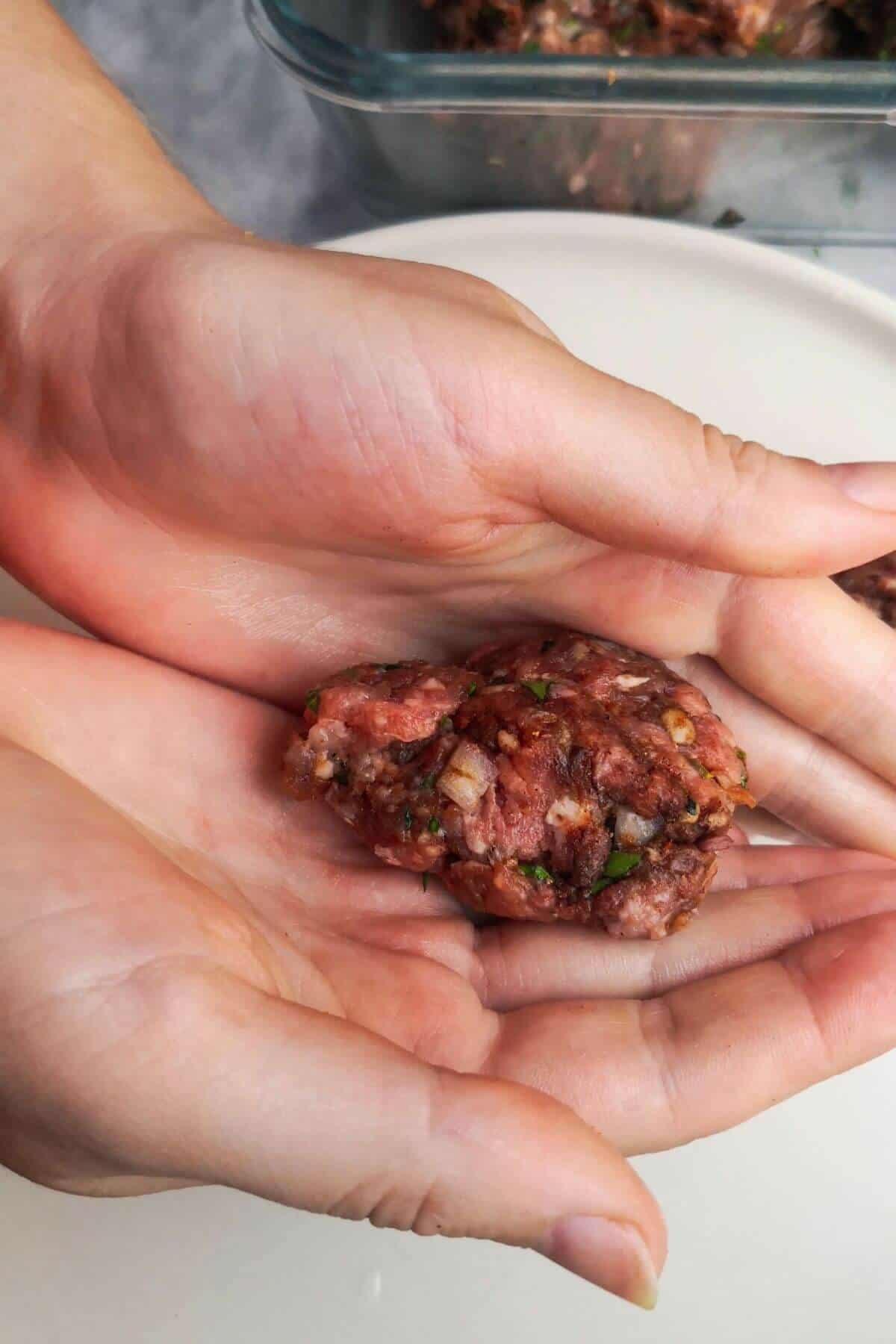 2 hands holding up a piece of lamb kofta mix with container of the mix in the background.