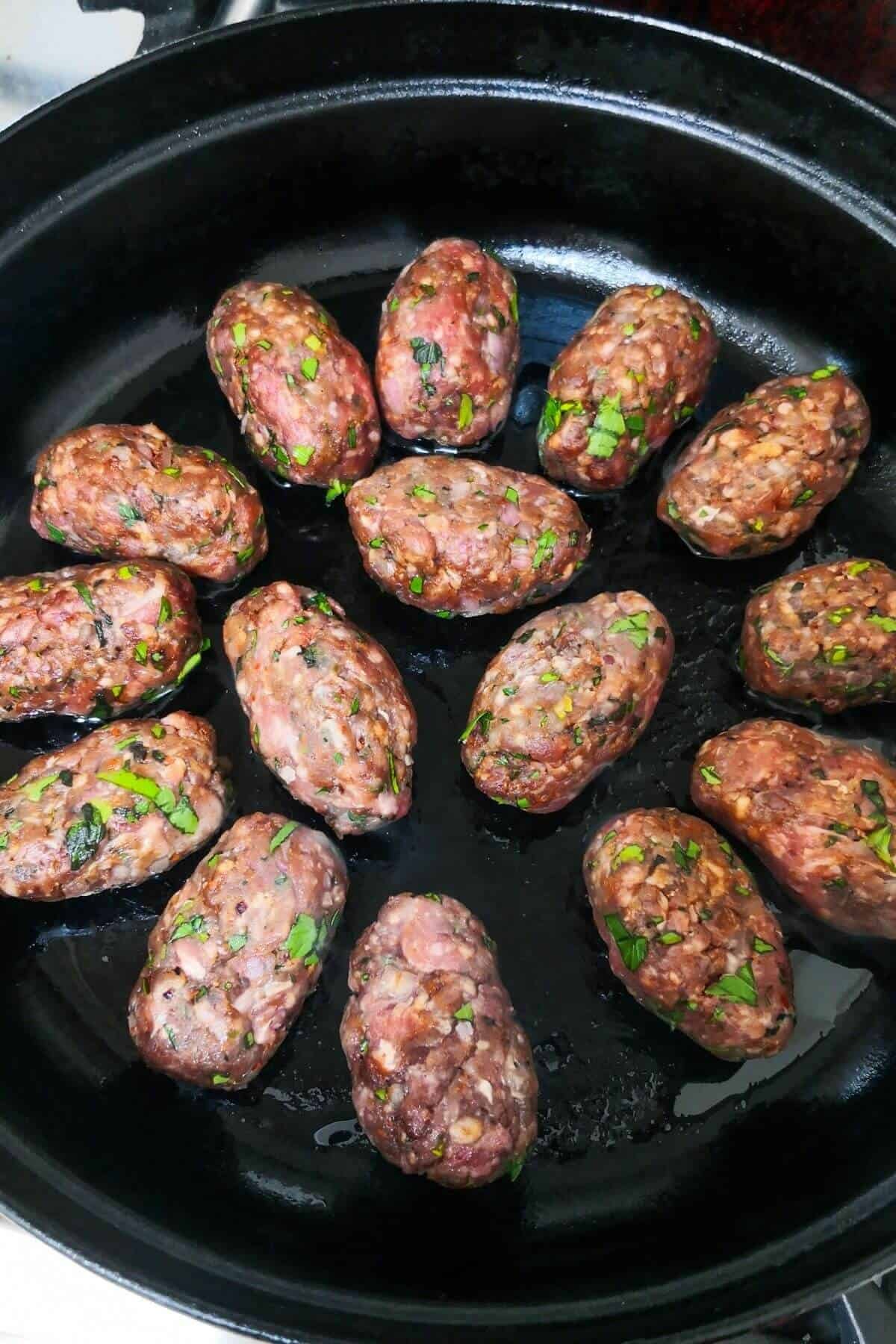 Lamb kofta cooking in a black skillet on the stove.
