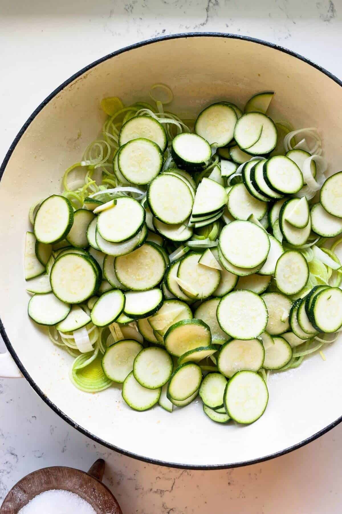 Sliced leeks and zucchini in a large white pot.