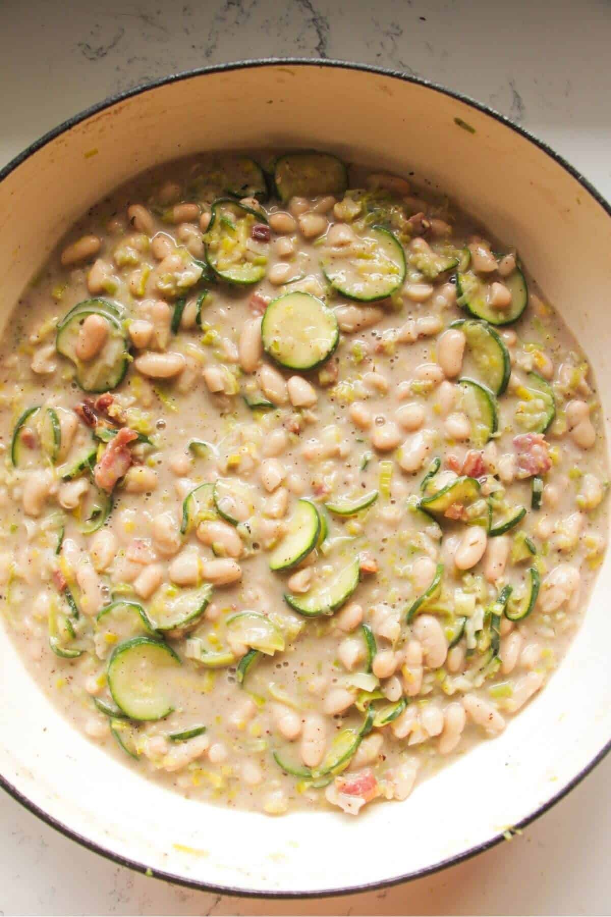 Creamy leek and zucchini beans in a large pot with bacon added.