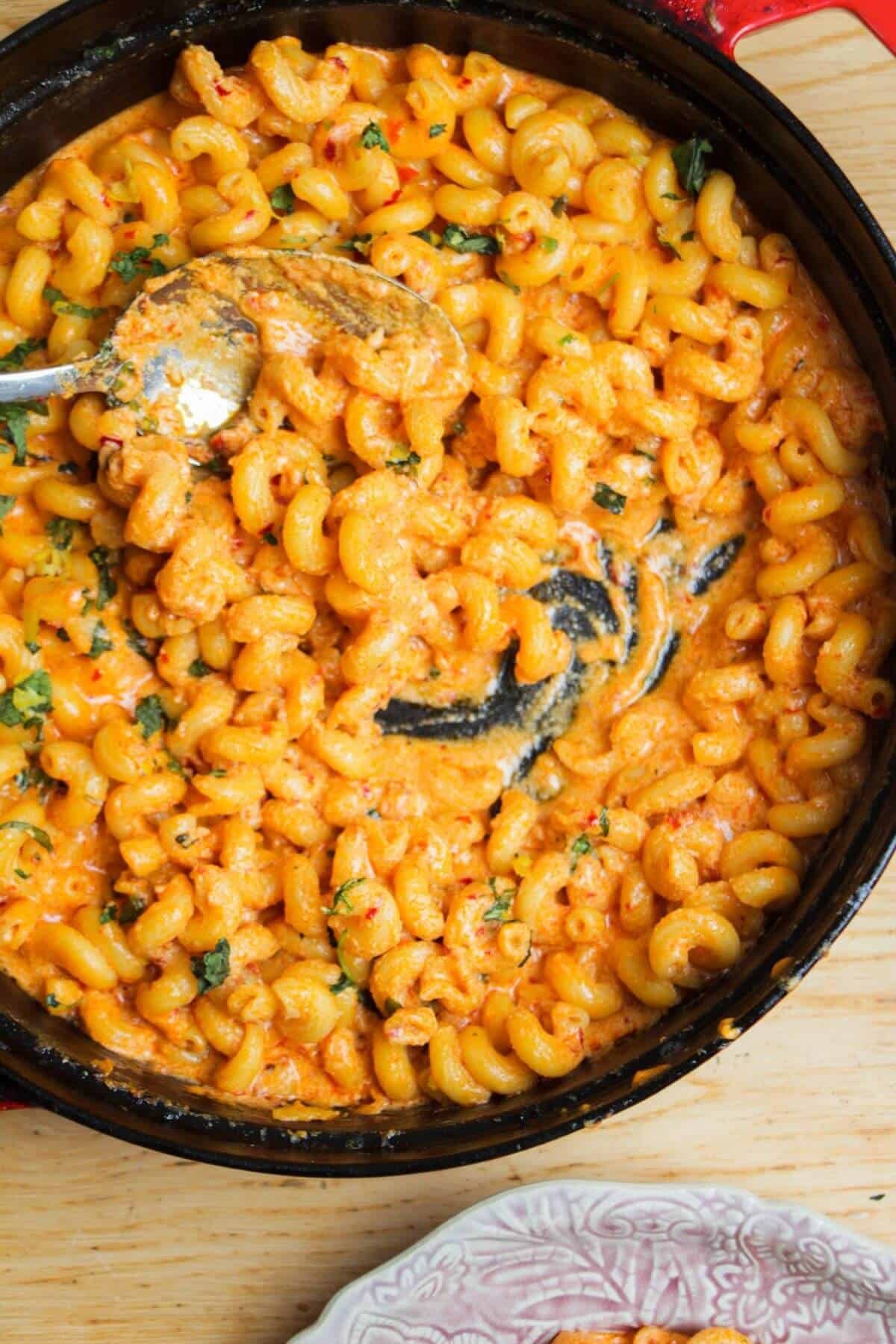 Spicy mac and cheese in a large black skillet with a silver spoon inside.