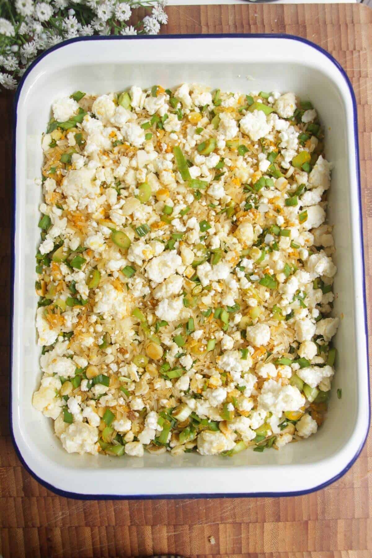 Cheese topped rice and herbs in a white tin.