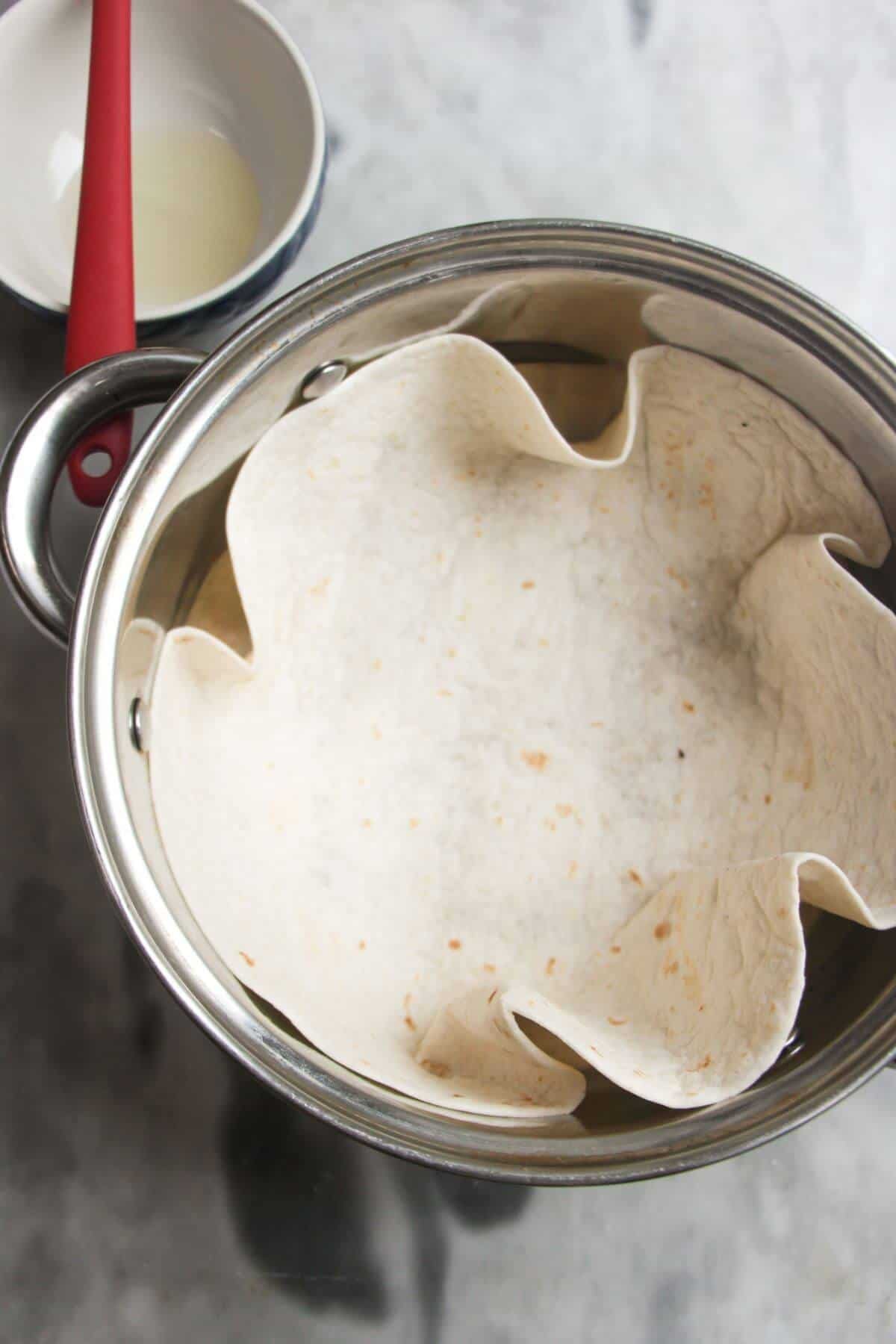 Tortilla inside a small silver pot with small bowl of oil in the background.