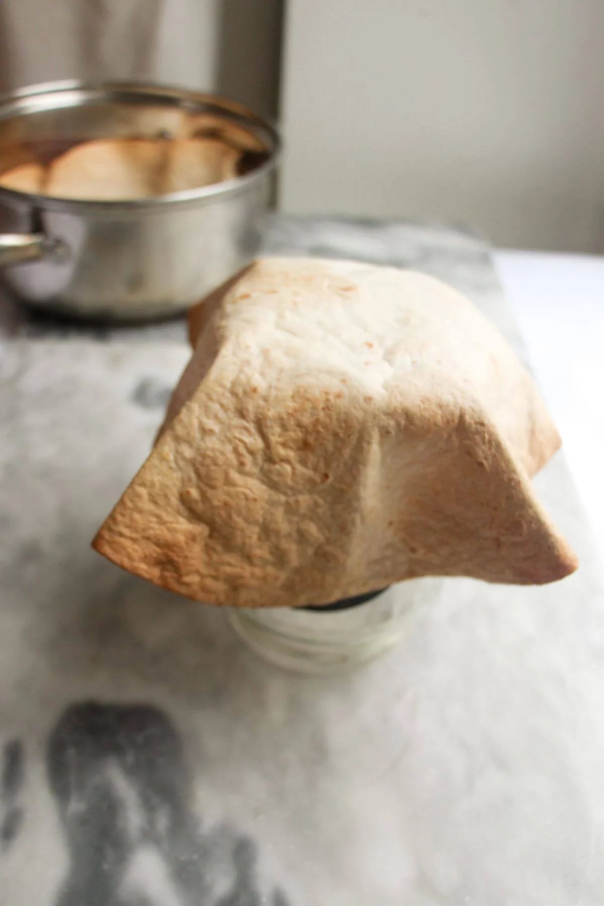 Crispy taco shell draped over a large glass jar with small silver pot in the background.