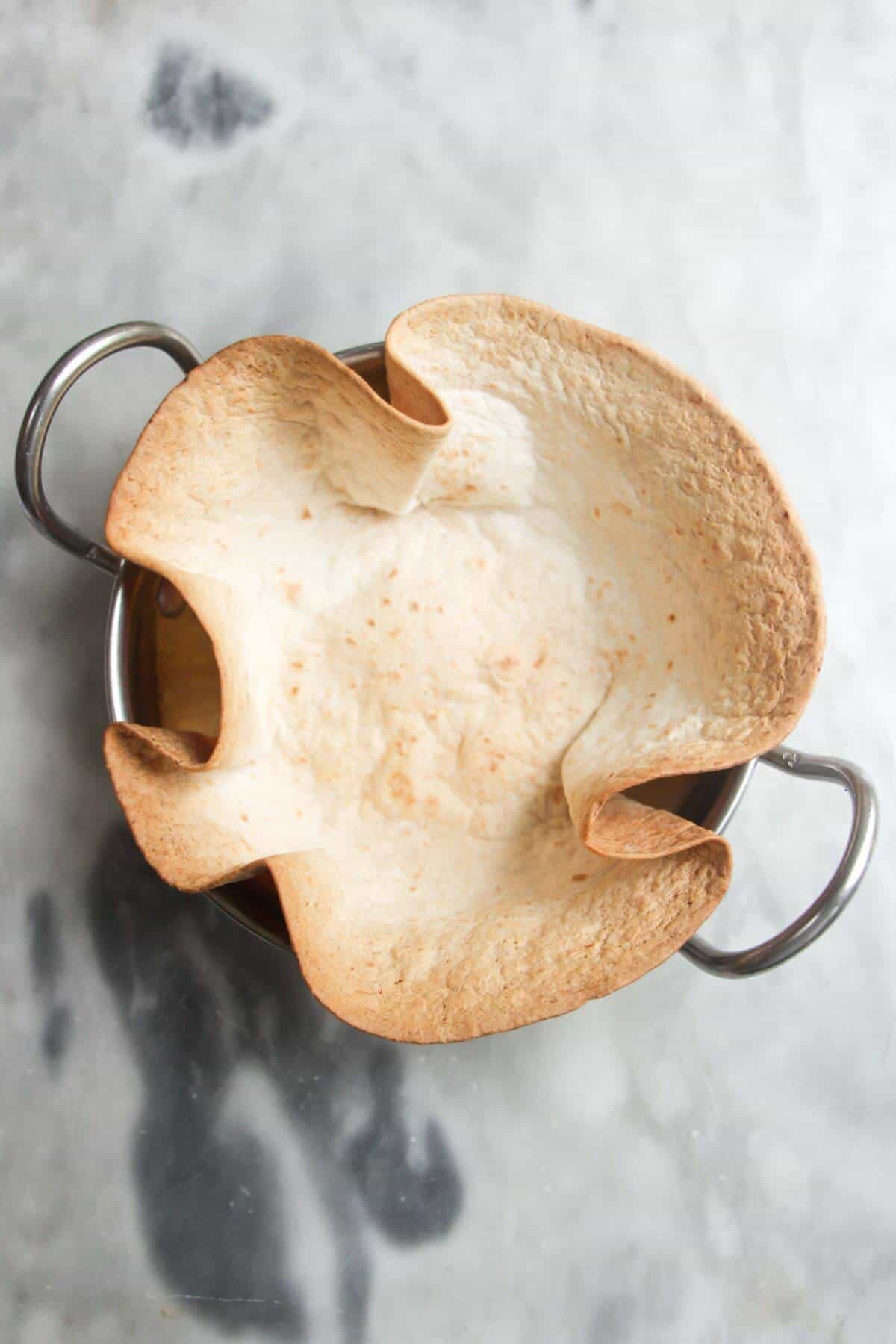 Crispy taco shell inside a small silver bowl on a grey marble background.