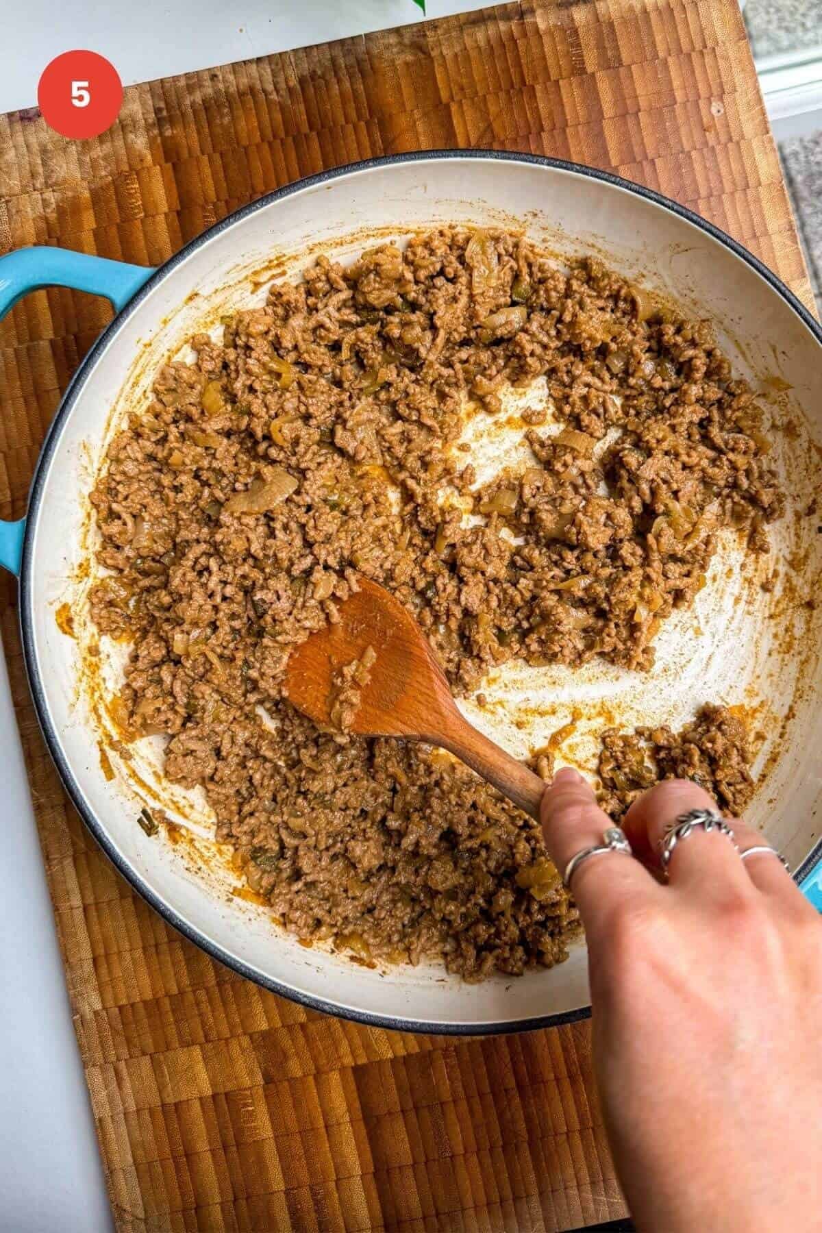 Stirring cheeseburger beef topping in a pan.