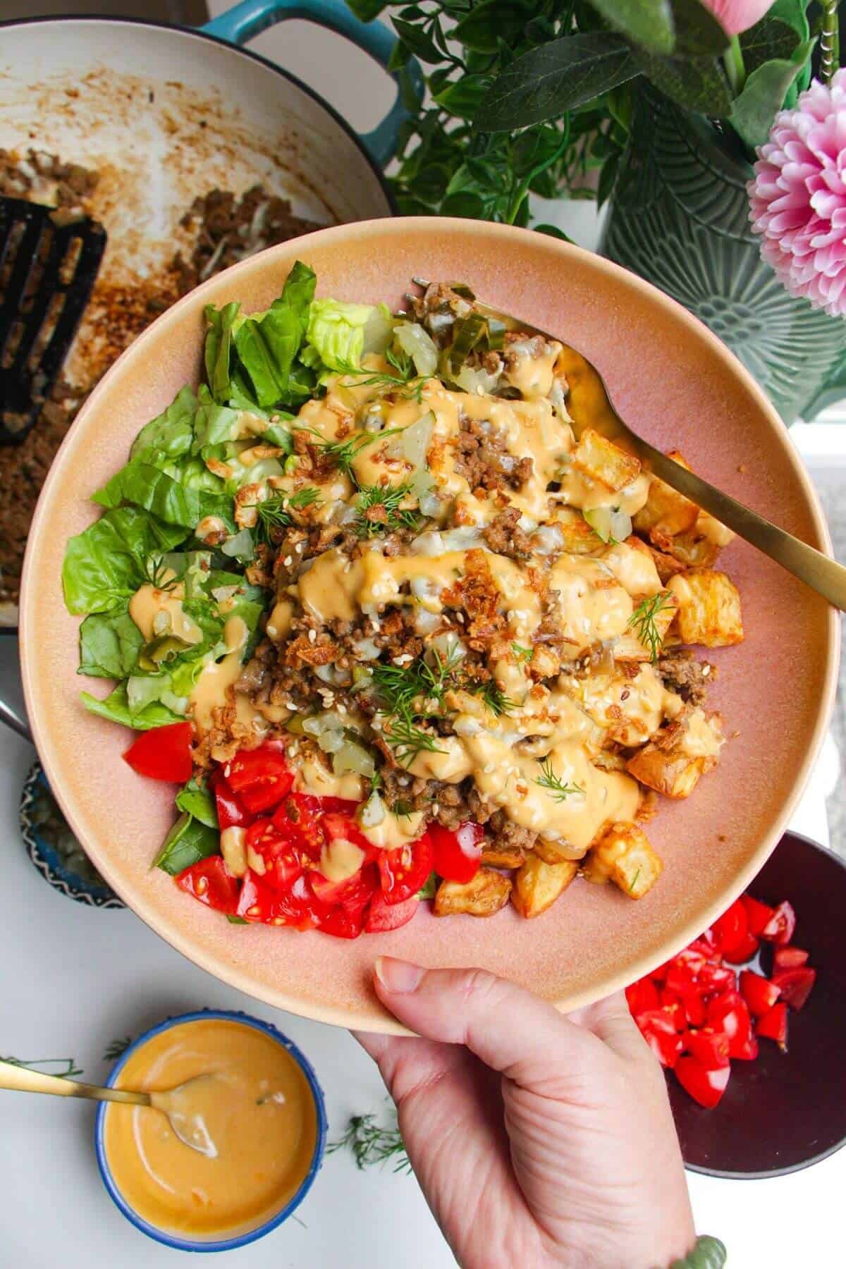 Holding loaded cheeseburger bowls drizzled with burger sauce.