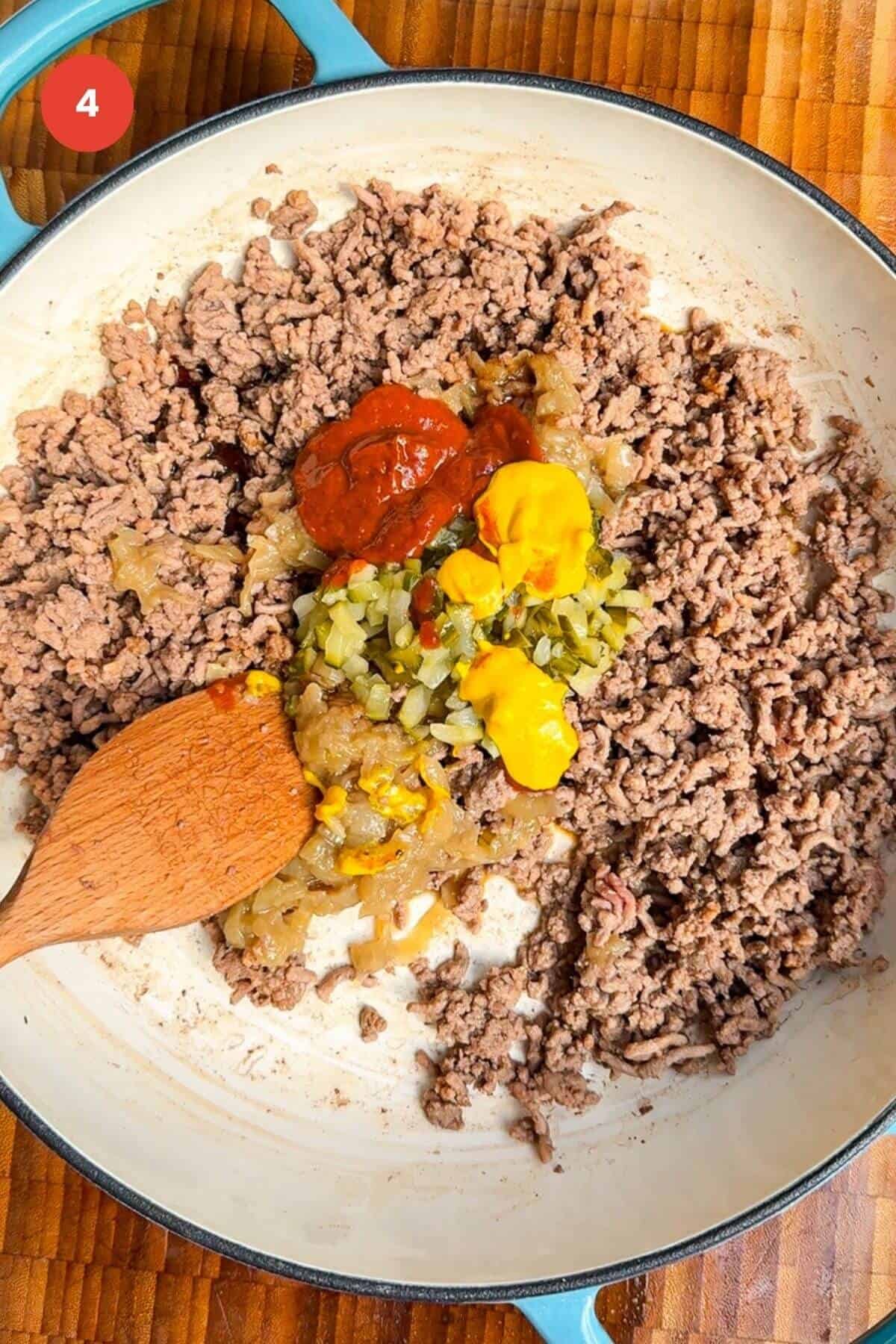 Ground beef browned in a pan, with ketchup, mustard and pickles.