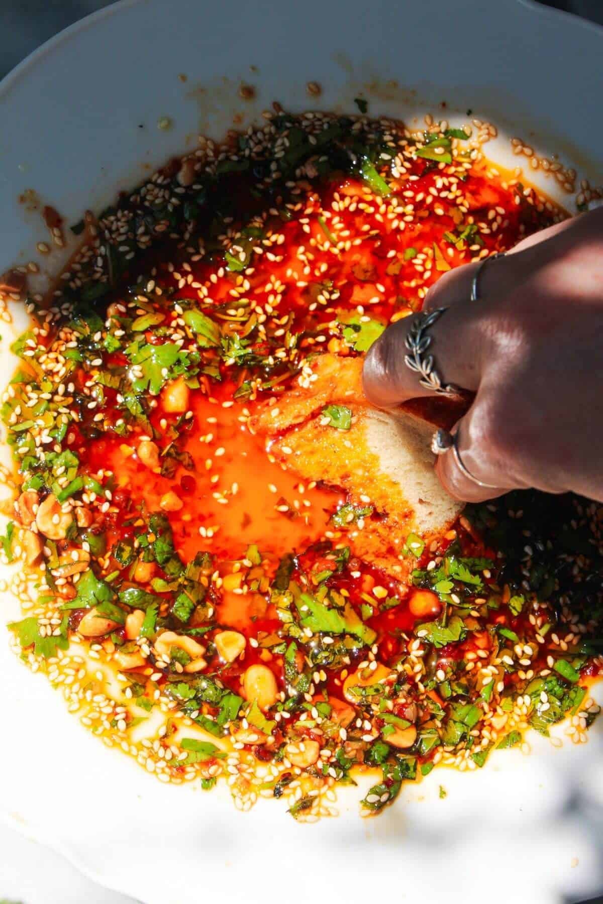 Hand sweeping bread through sweet chilli dipping oil.