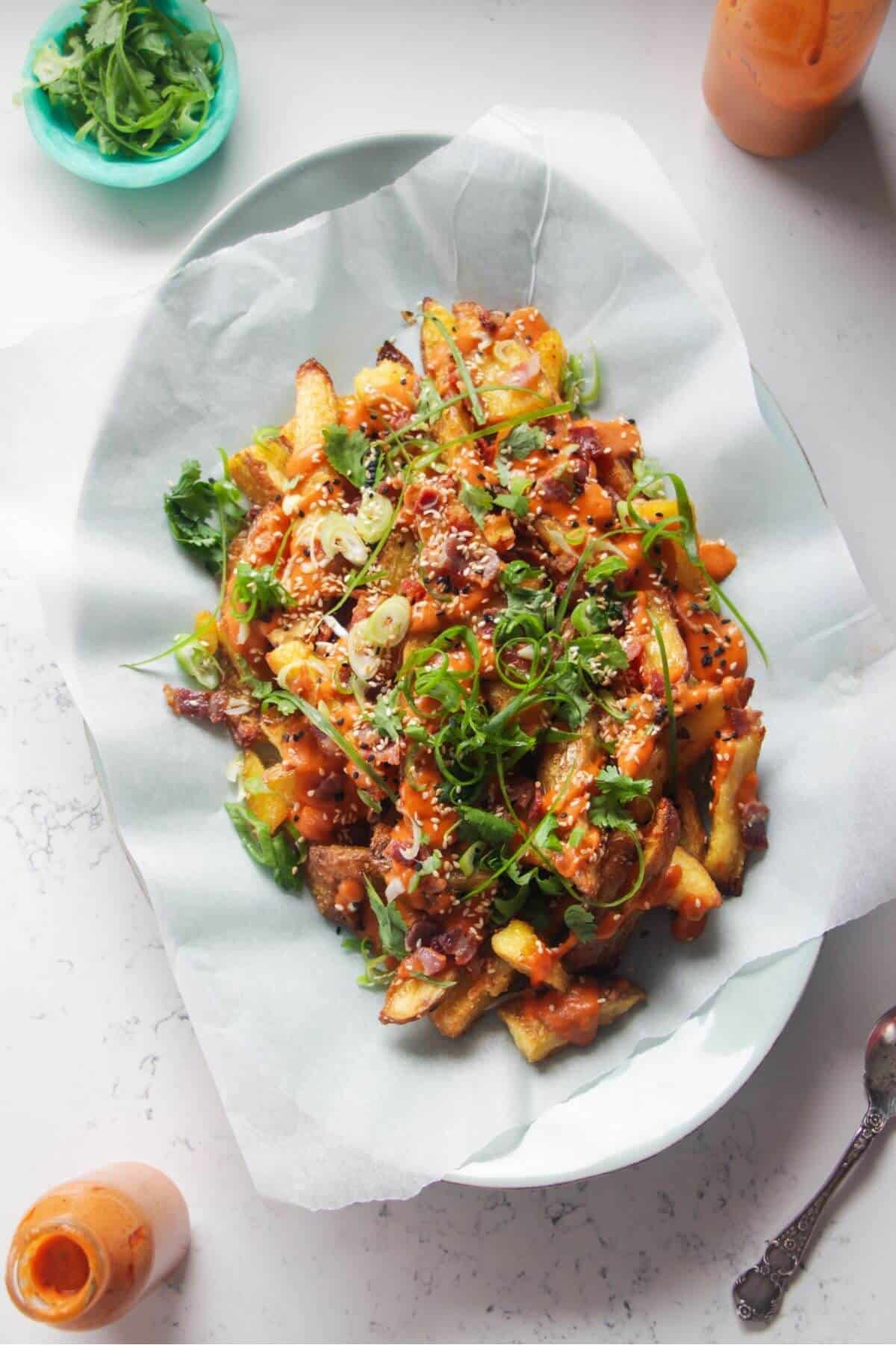 Loaded potato wedges on a large oval white plate with small jug of gochujang bechamel on the side.