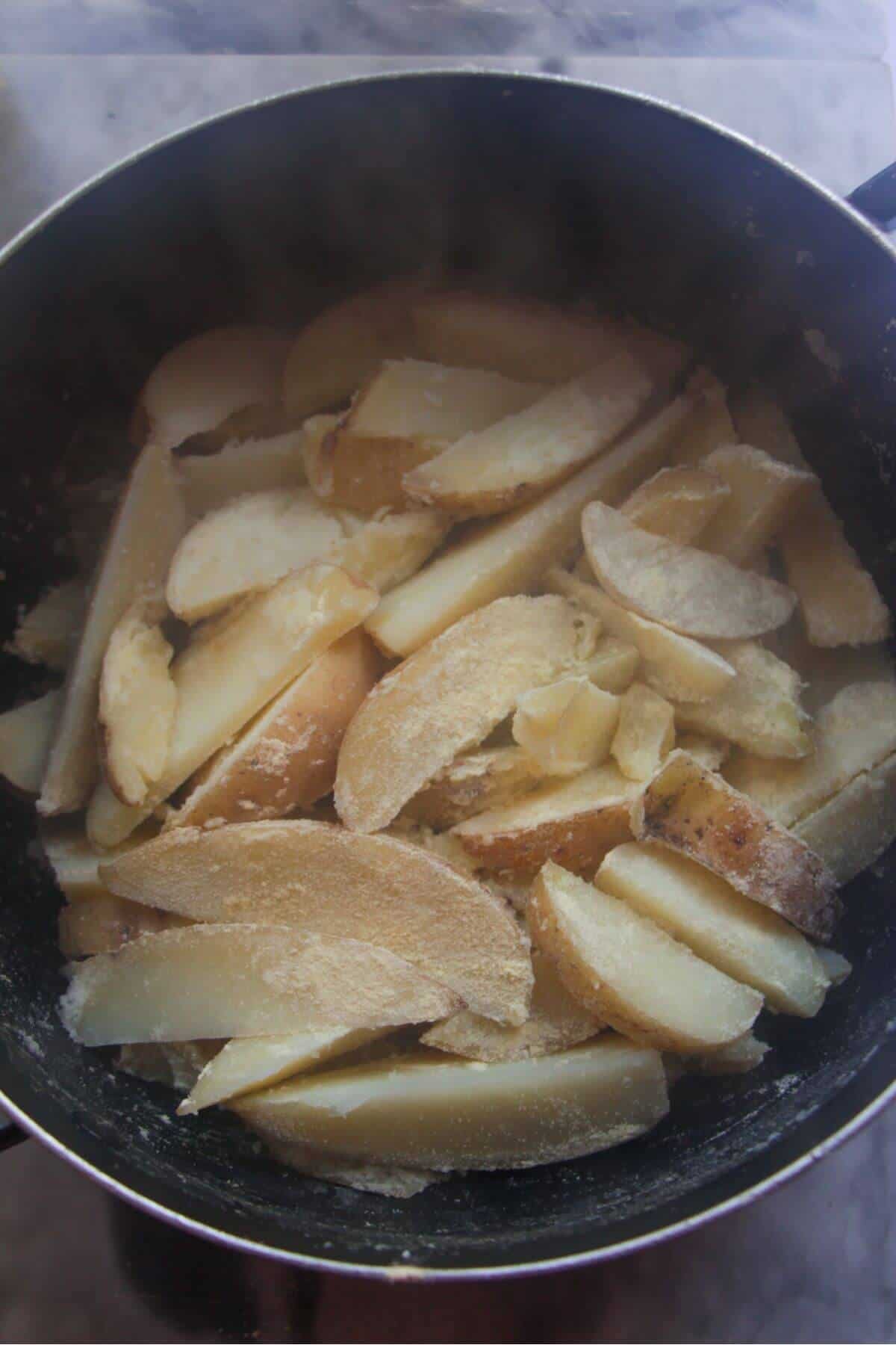 Wedges tossed with polenta in a large black pot.
