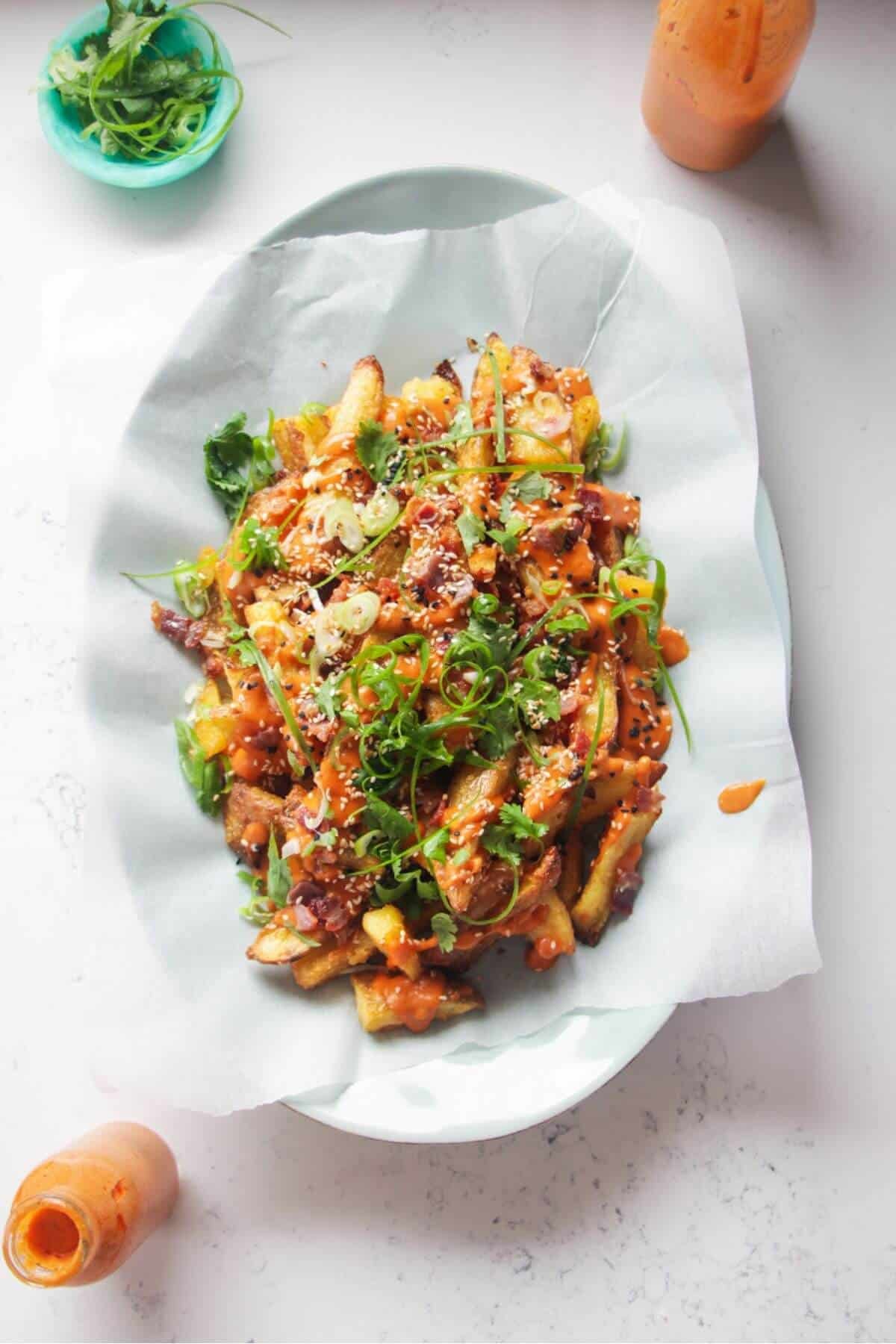 Loaded potato wedges on a large oval white plate with small jug of gochujang bechamel on the side.