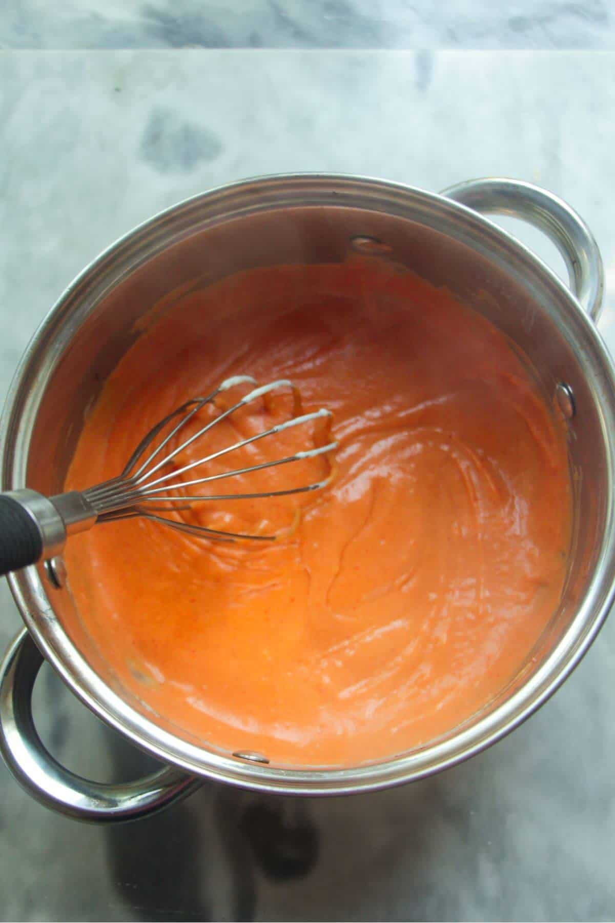 Whisking orange gochujang bechamel in a small silver pot.