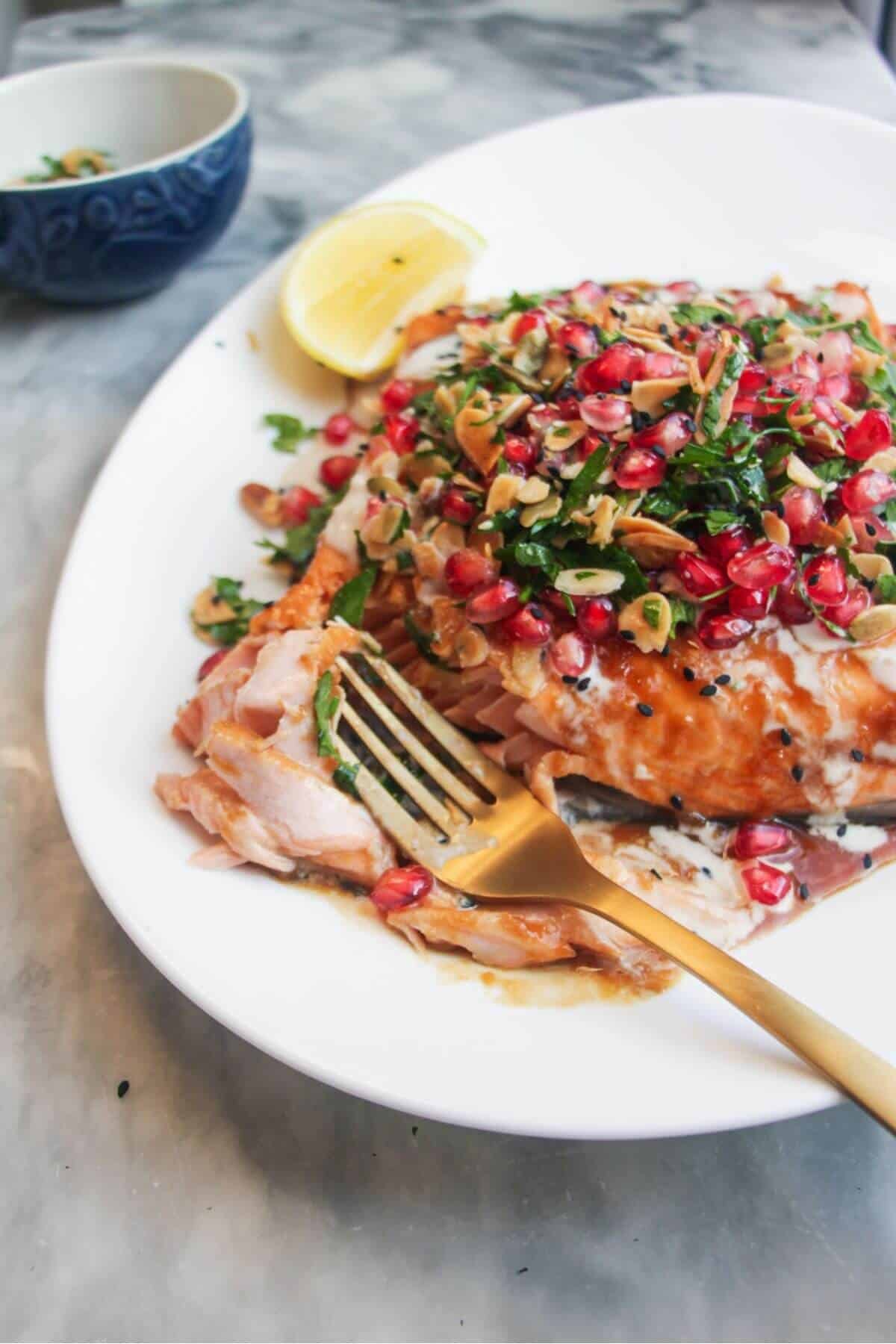 Close up of a fork flaking pieces of salmon from a salmon fillet, topped with pomegranate salsa.