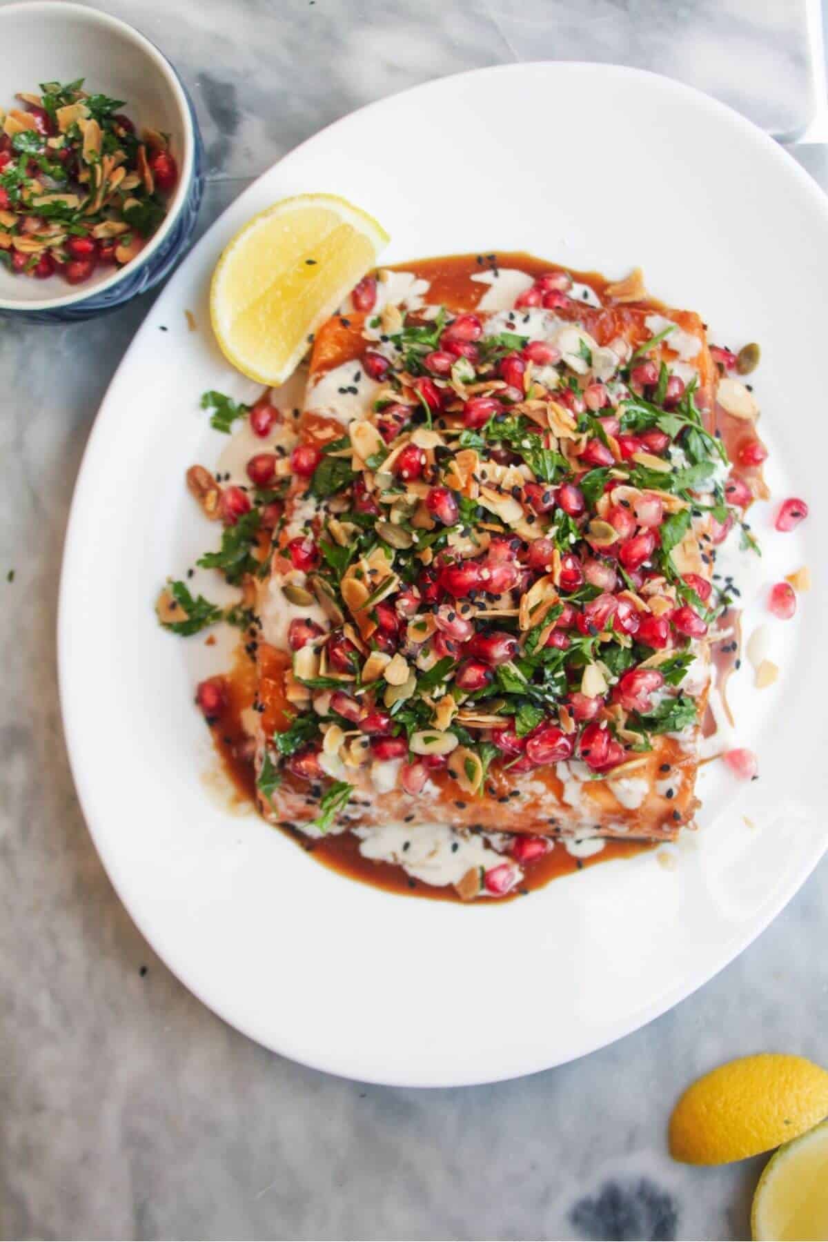 Maple miso glazed salmon fillet with pomegranate almond salsa, with lemon wedges on the side.