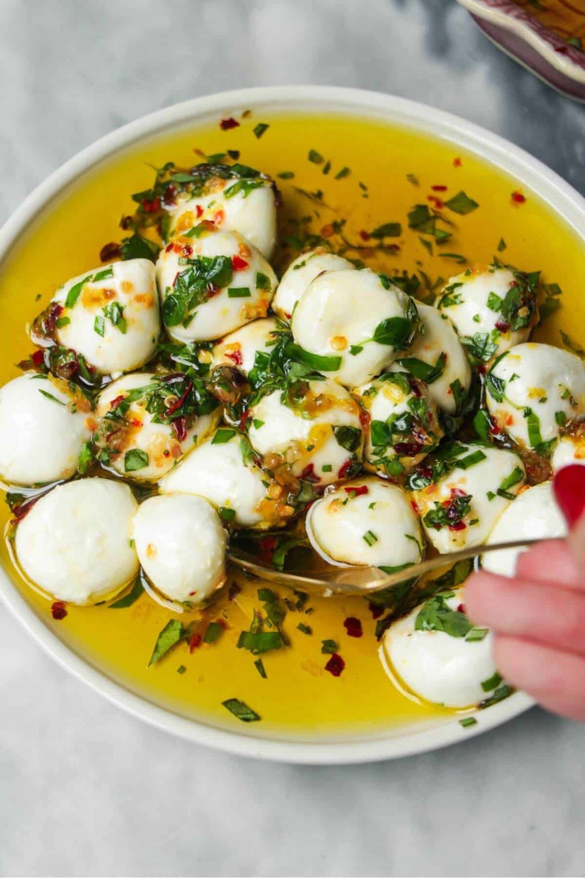 Mixing mozzarella balls through marinade in a small white plate.