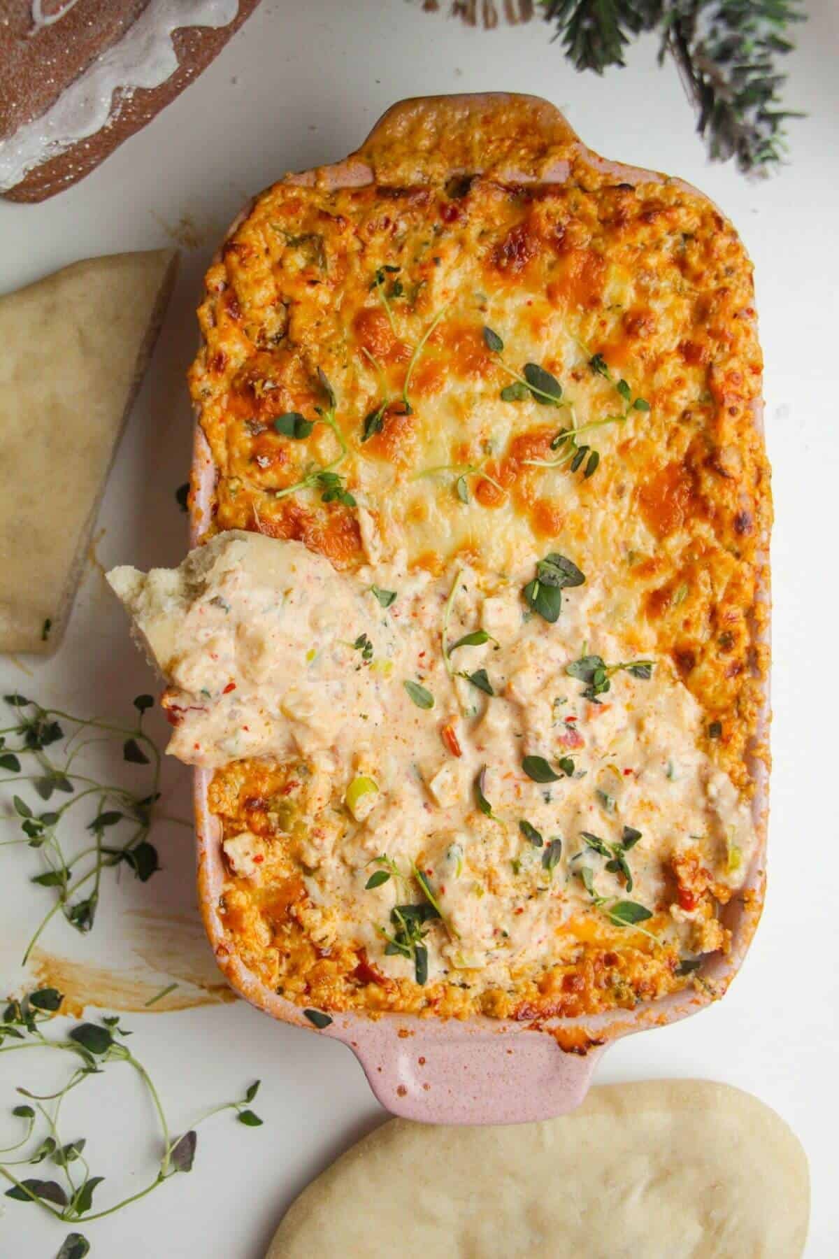 Pita bread dipped into baked dip in a baking dish.