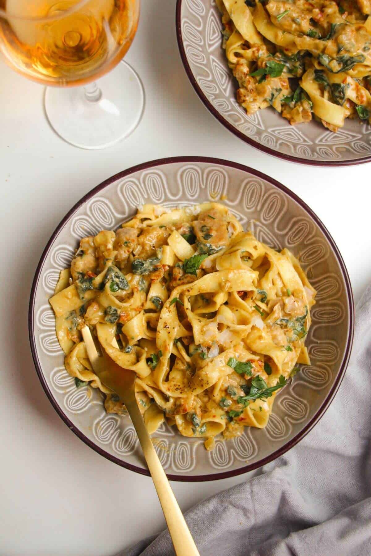 Two bowls of fettuccine on a white background, with a glass of wine.