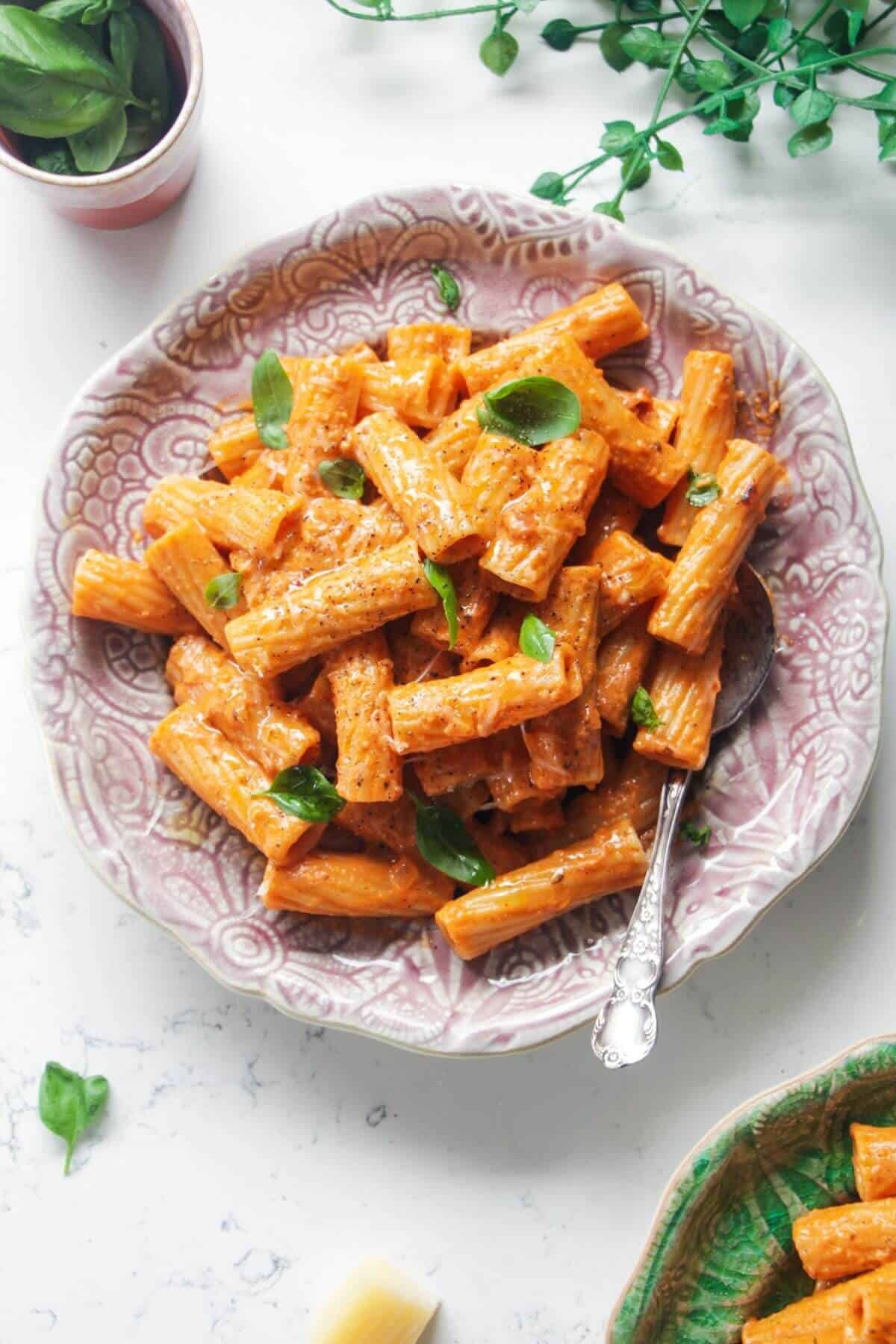 Spicy rigatoni on a pink plate with another small plate of rigatoni next to it.
