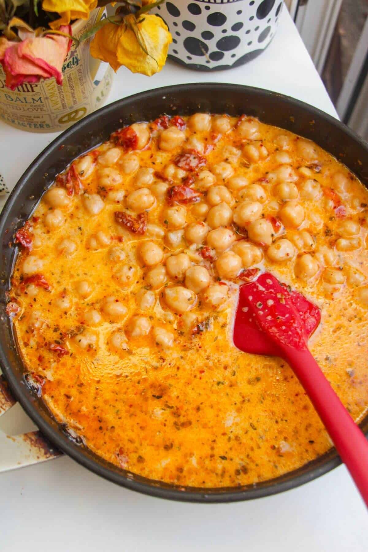 Stirring creamy sundried tomato sauce through chickpeas in a pan.