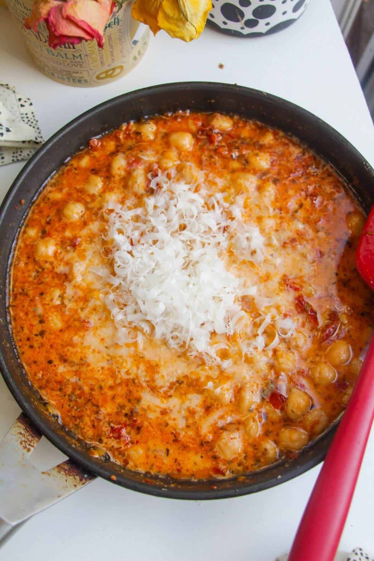 Grated parmesan added to creamy sundried tomato chickpeas in a pan.