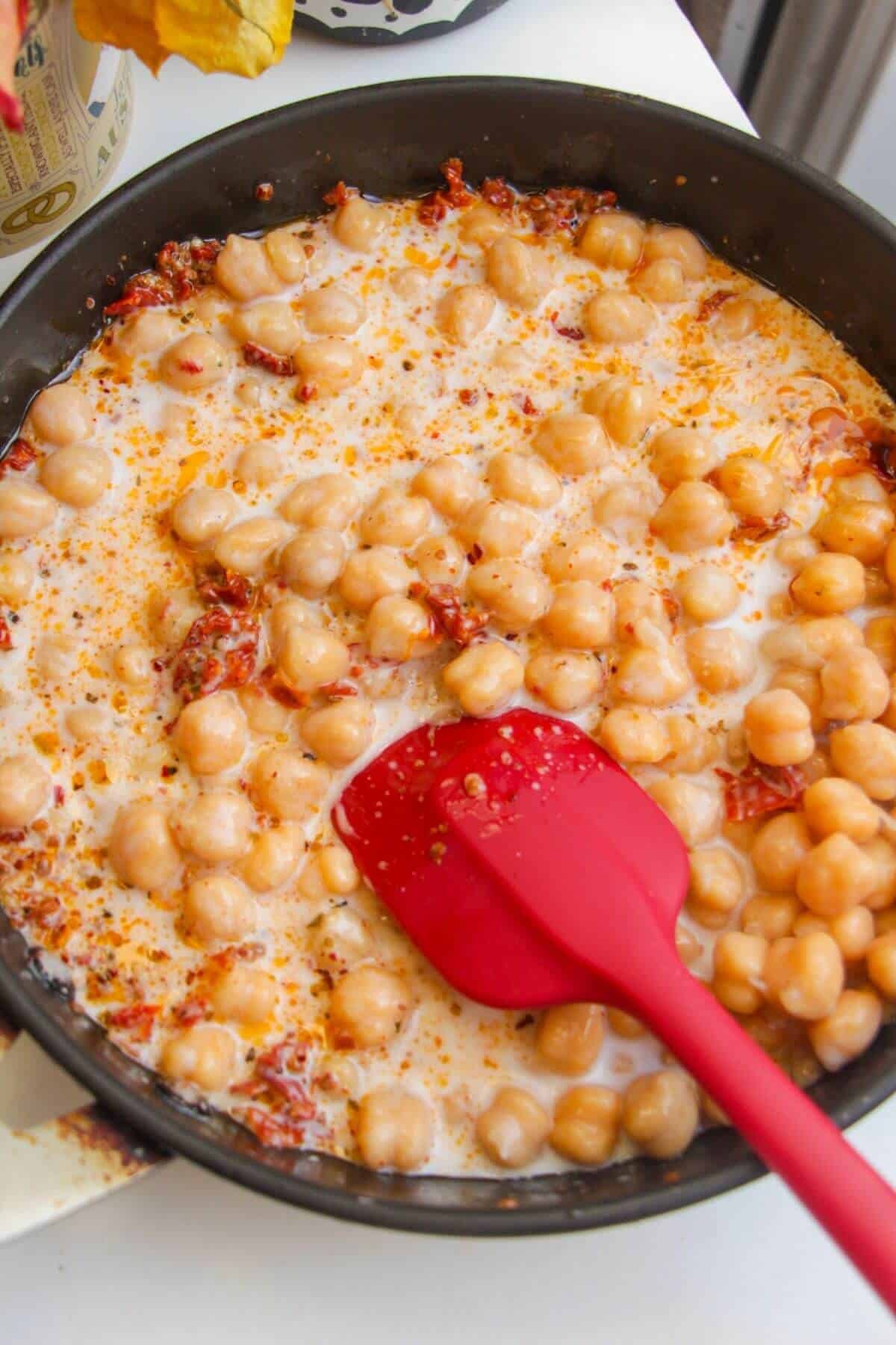 Coconut milk added to chickpeas in a small pan.