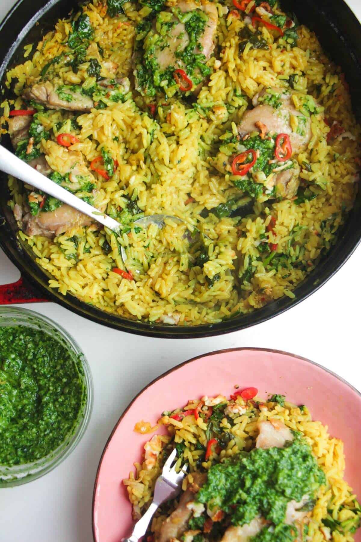 Pesto topped chicken with rice in a large pot with pink plate and pesto on the side.