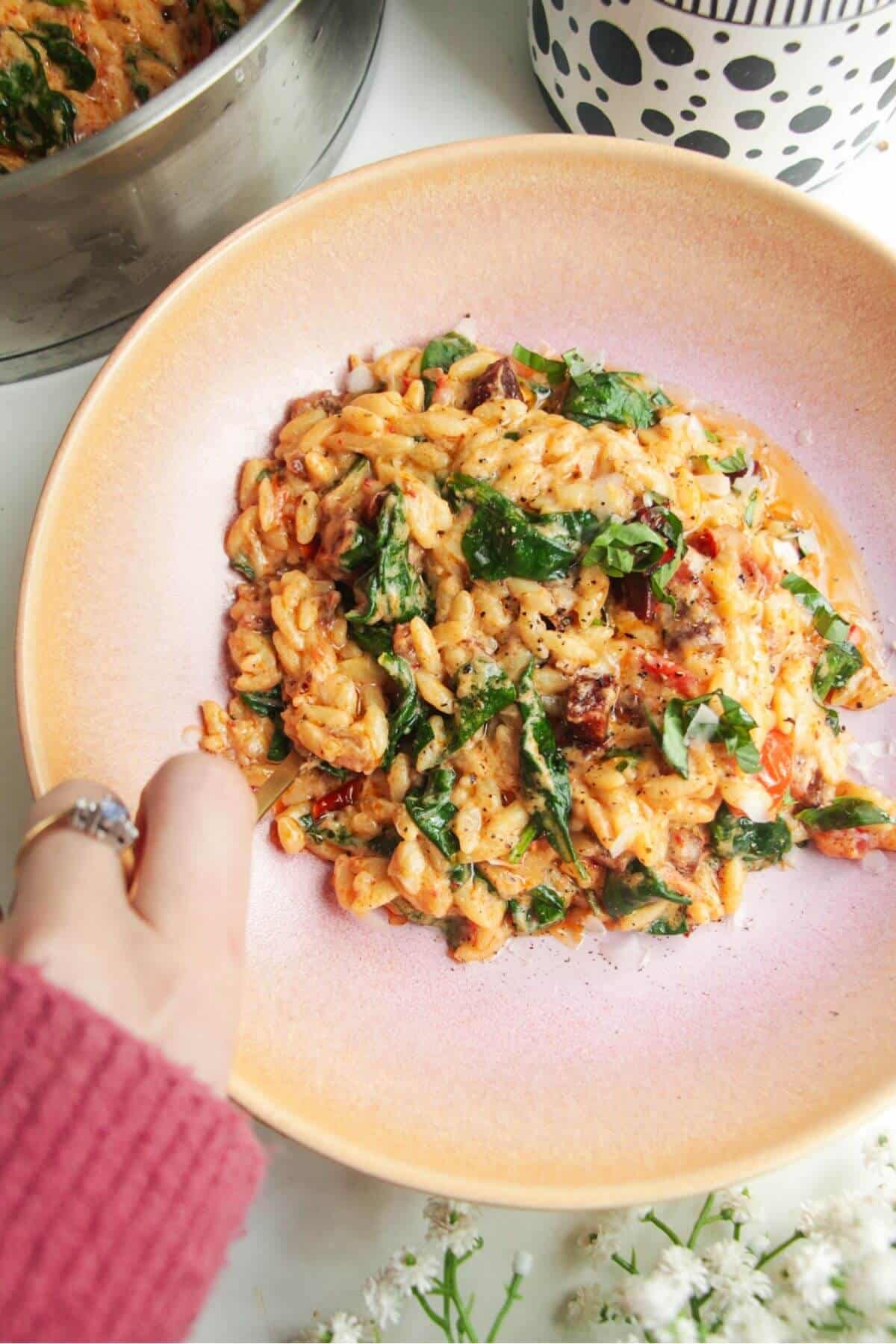 Marry Me orzo in a pink bowl with a pan in the background.
