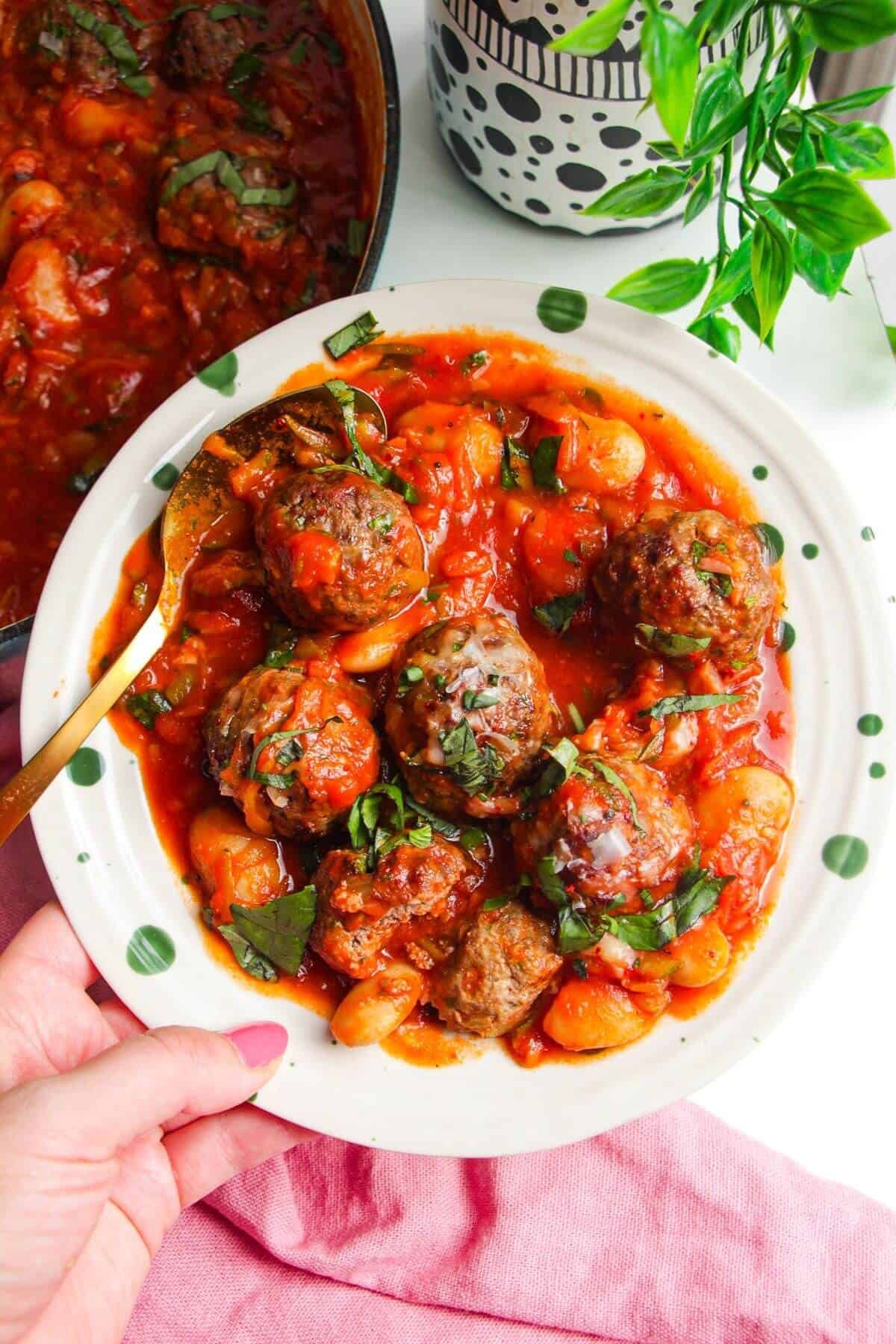 Holding plate with beef meatballs and butter beans in tomato sauce.