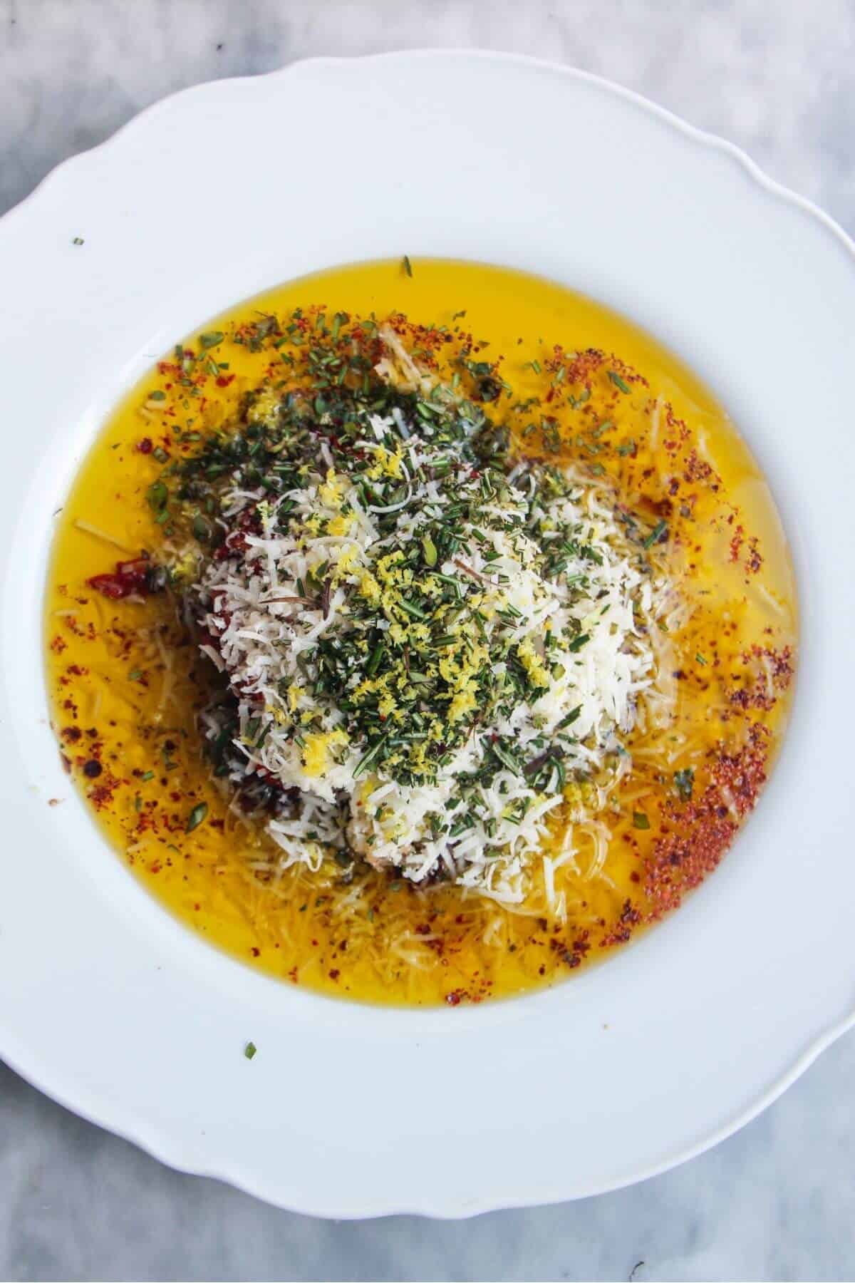 Ingredients for olive oil dip piled on top of eachother on a large white plate.