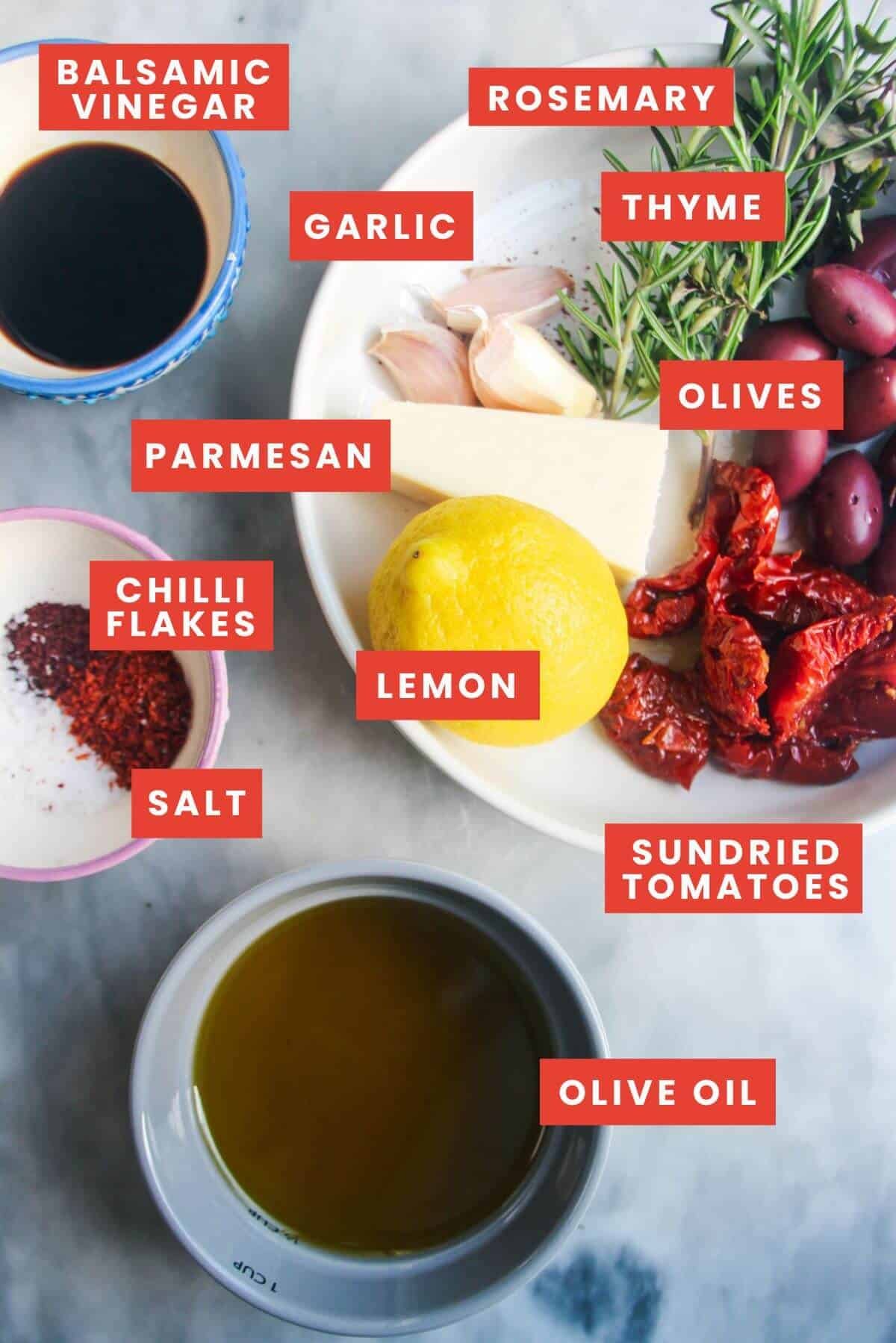 Ingredients for loaded olive oil dip laid out on a grey marble background and labelled.