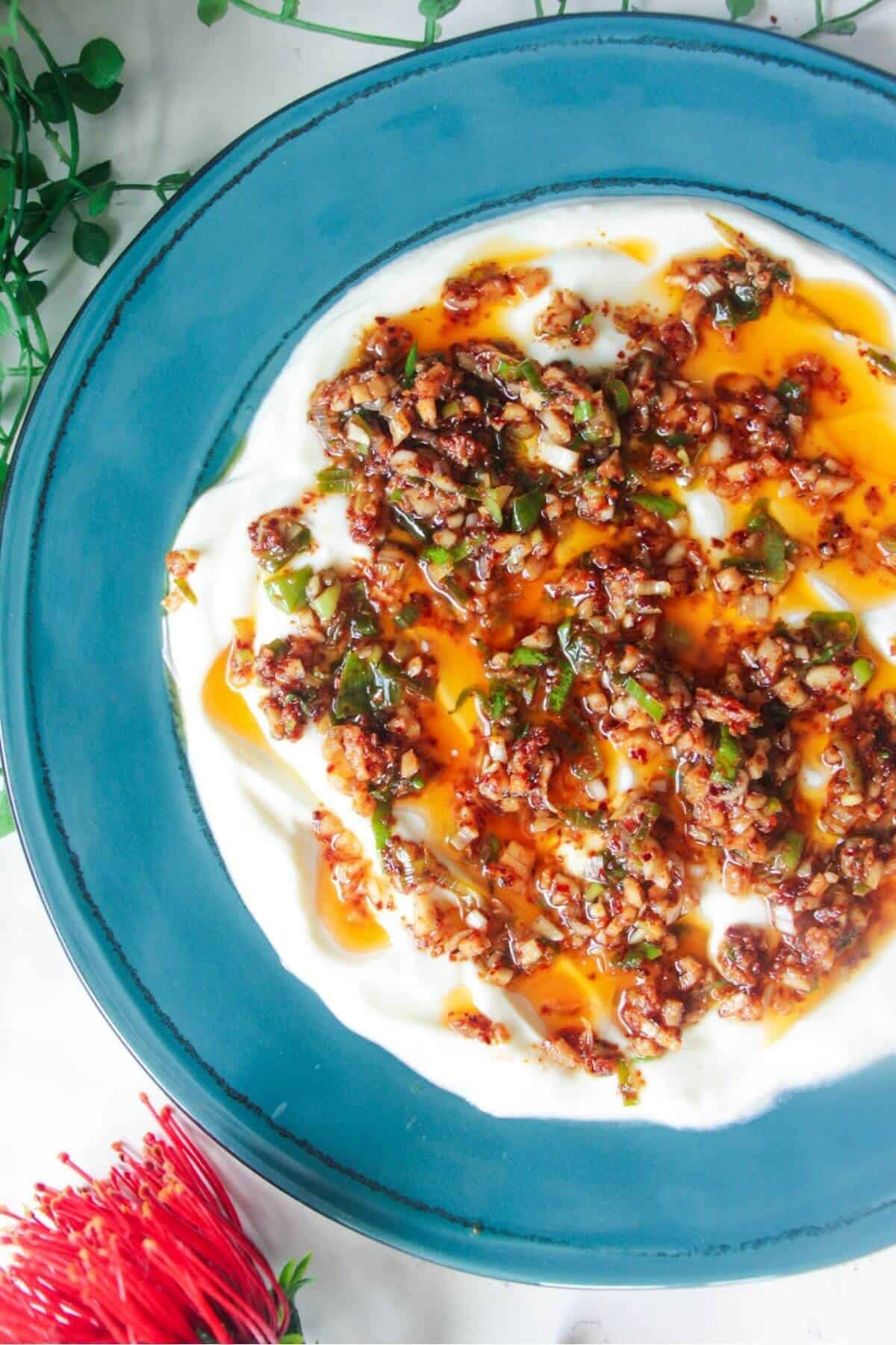 Sizzling oil on top of creamy Greek yogurt on a teal plate.