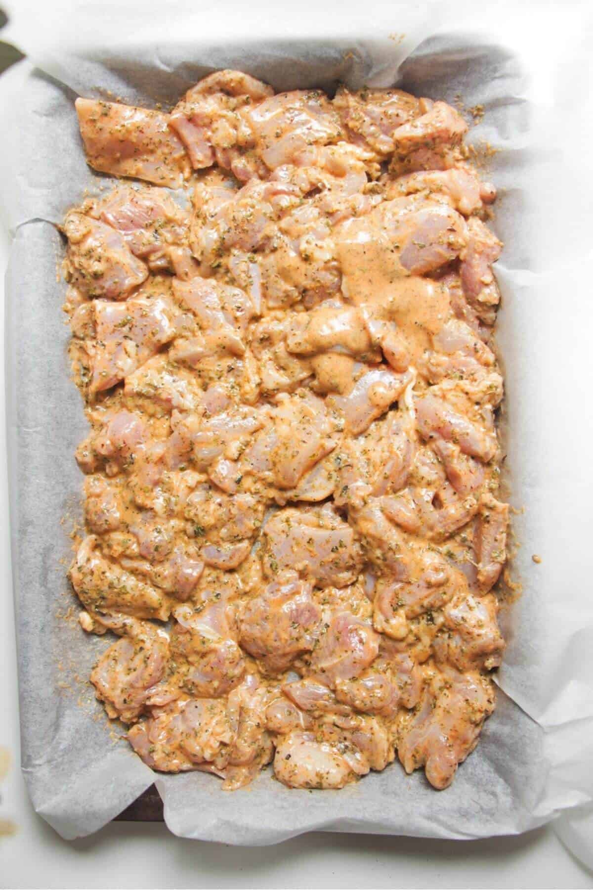 Diced marinated chicken thighs on a lined oven tray.