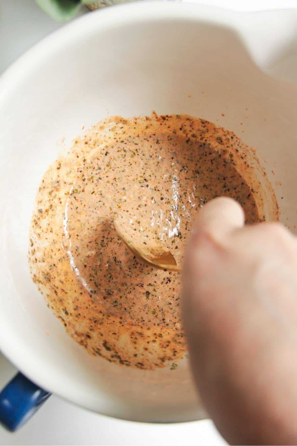 Hand holding spoon mixing gyros chicken marinade in a bowl.