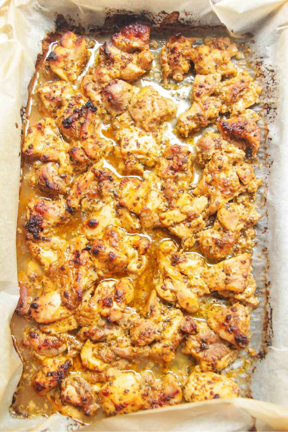 Charred, cooked chicken on a lined oven tray.