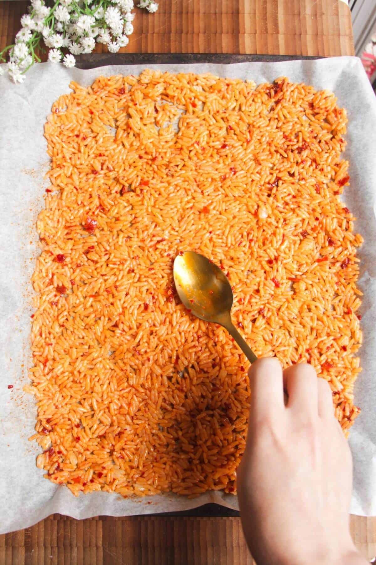 Spreading spicy rice on a lined oven tray.