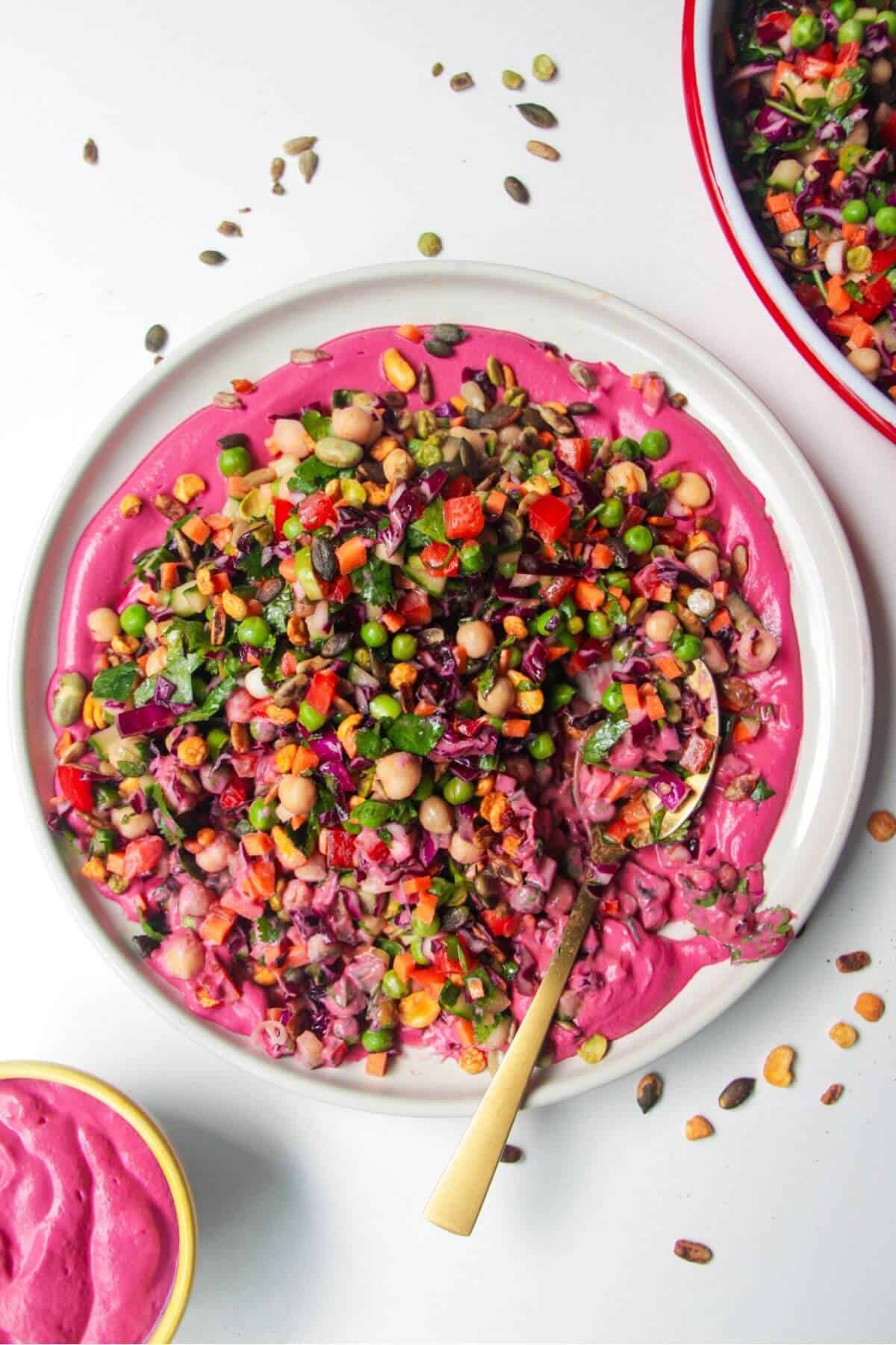 Rainbow chopped salad on pink tahini sauce on a white plate, with extra sauce on the side.
