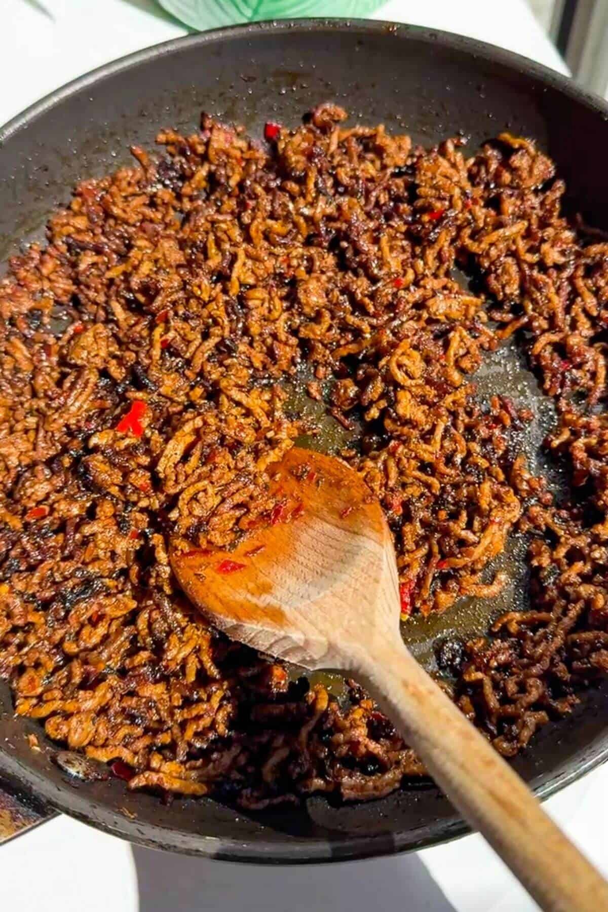 Stirring sticky ground beef in pan.